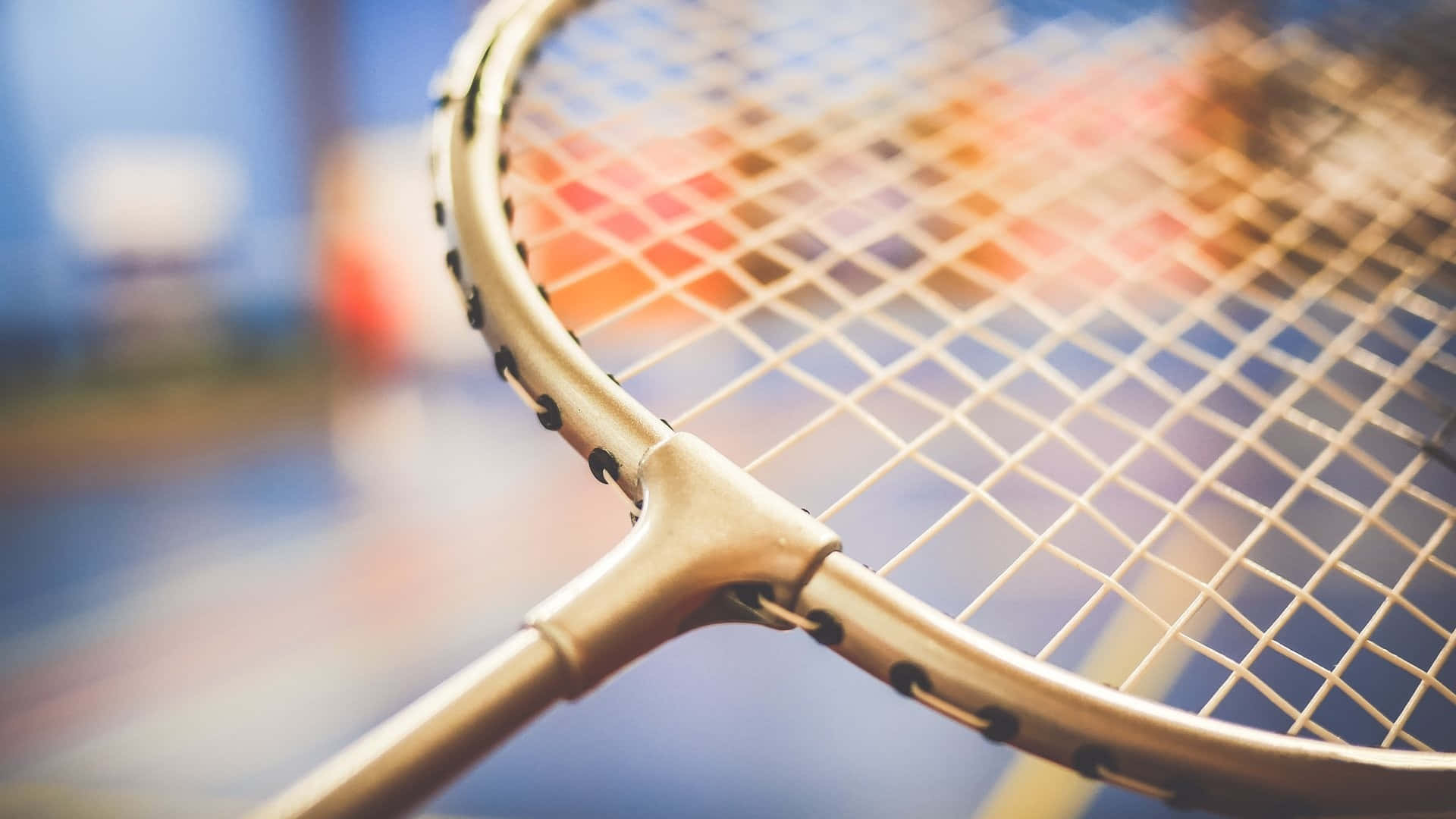 Best Badminton 桌布 壁紙 — 金色網球拍的近距離特寫，背景為模糊多彩的球場。