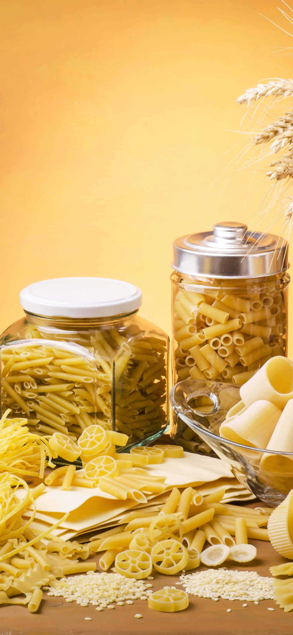 food iPhone 桌布 壁紙 — 金色義大利麵從玻璃罐和碗中溢出，襯以溫暖的黃色背景和小麥莖。