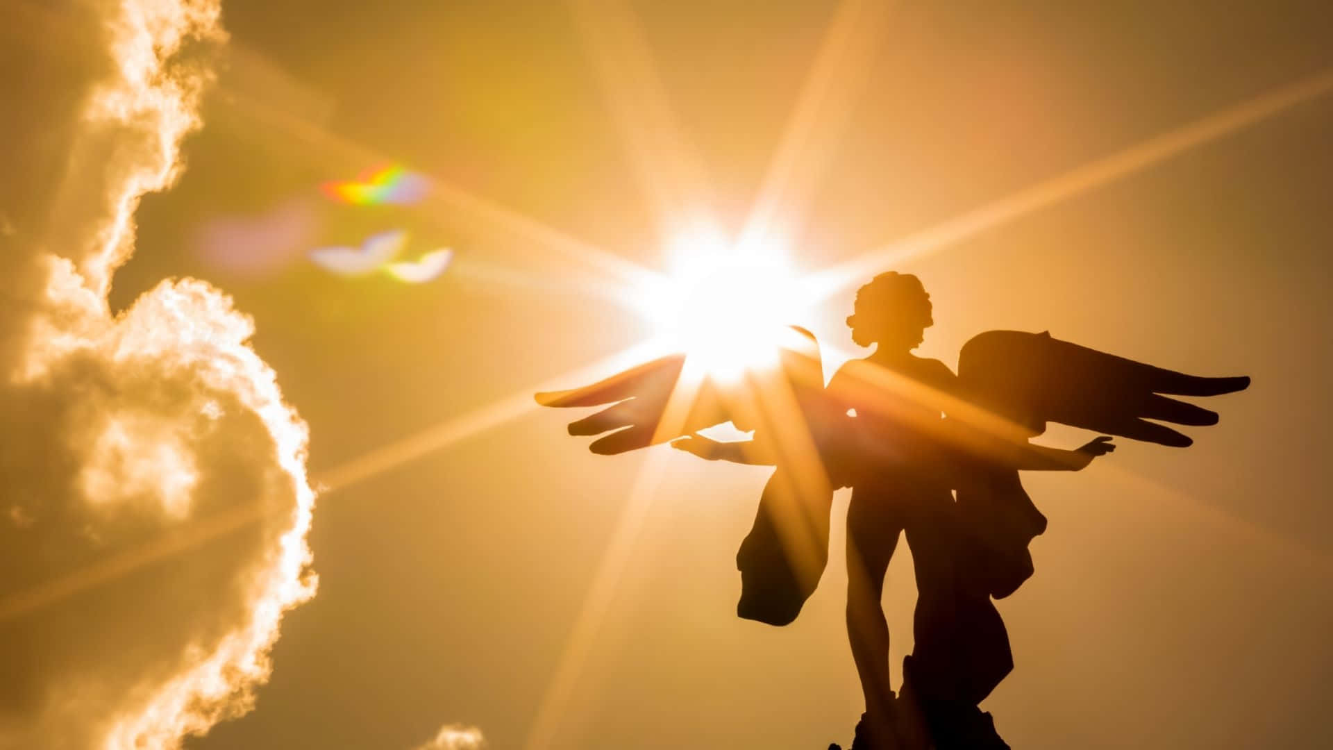 天使 桌布 壁紙 — 金色翅膀的天使雕像在熾熱的太陽、放射狀鏡頭光暈和發光的雲彩襯托下形成剪影。