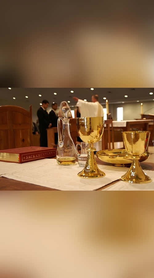 Sacrament 桌布 壁紙 — 金色聖杯和聖禮書放在教堂祭壇上，背景中一位神父正在主持禮拜。