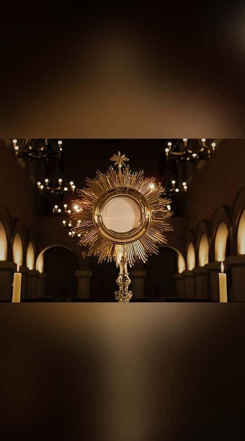 Sacrament 桌布 壁紙 — 金色聖體光在光線昏暗的大教堂中散發光芒，教堂內有拱形窗戶和懸掛的水晶吊燈。