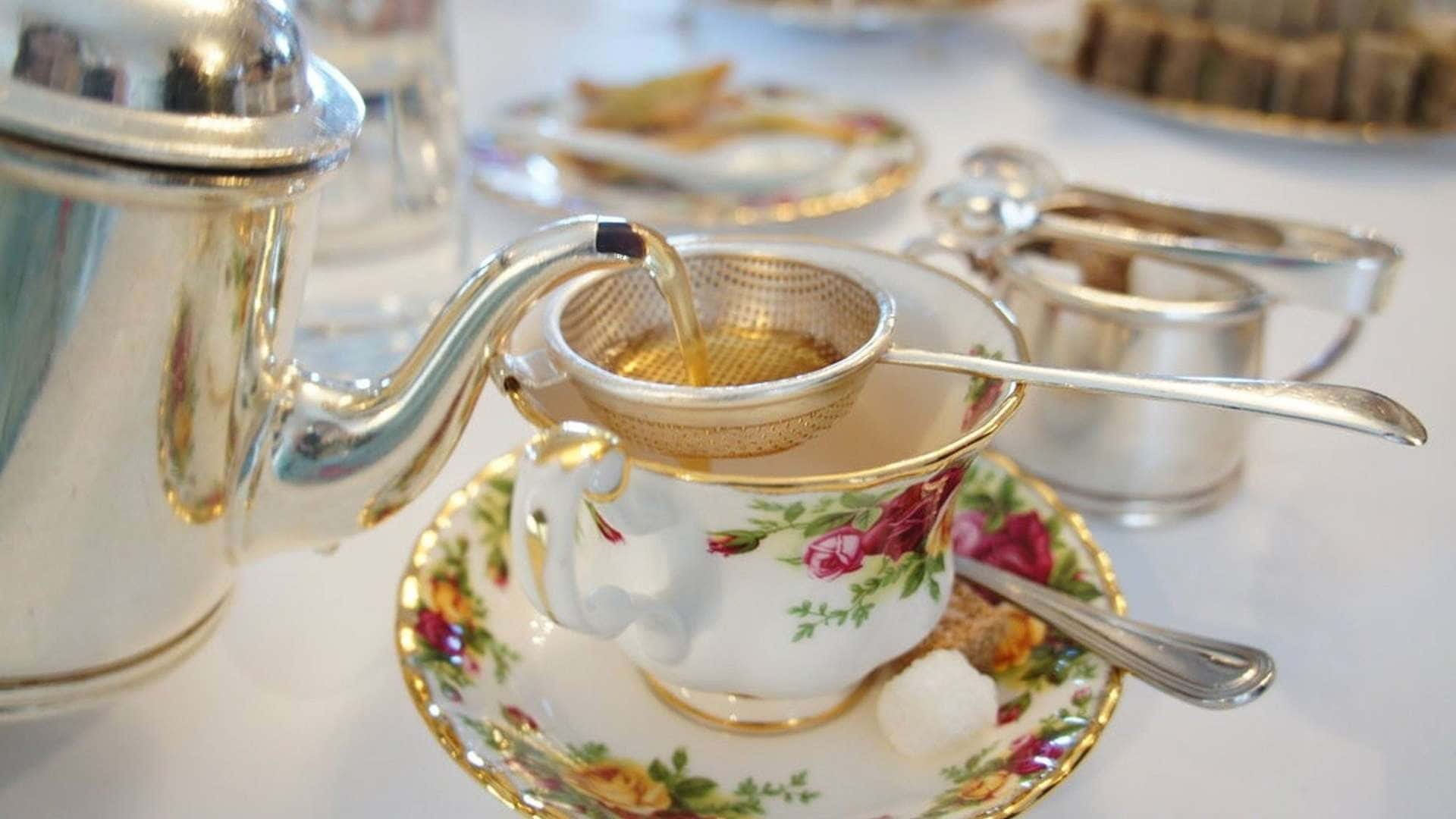 咖啡動圖 桌布 壁紙 — 金色茶湯透過濾網倒入花卉茶杯，旁邊有銀器和方糖。