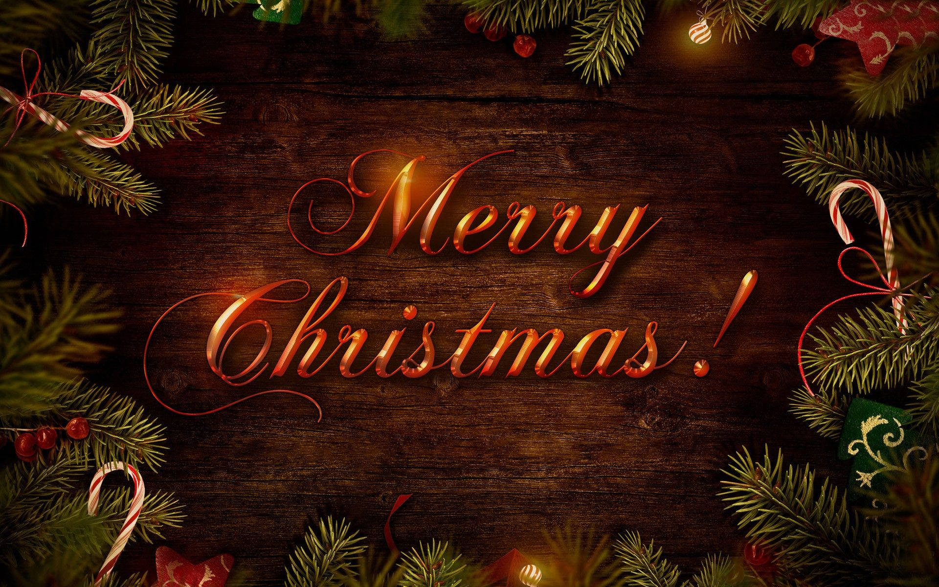 美麗聖誕 桌布 壁紙 — 金色草書Merry Christmas文字在深色木背景上溫暖發光，周圍環繞著松樹枝、拐杖糖和節日裝飾。