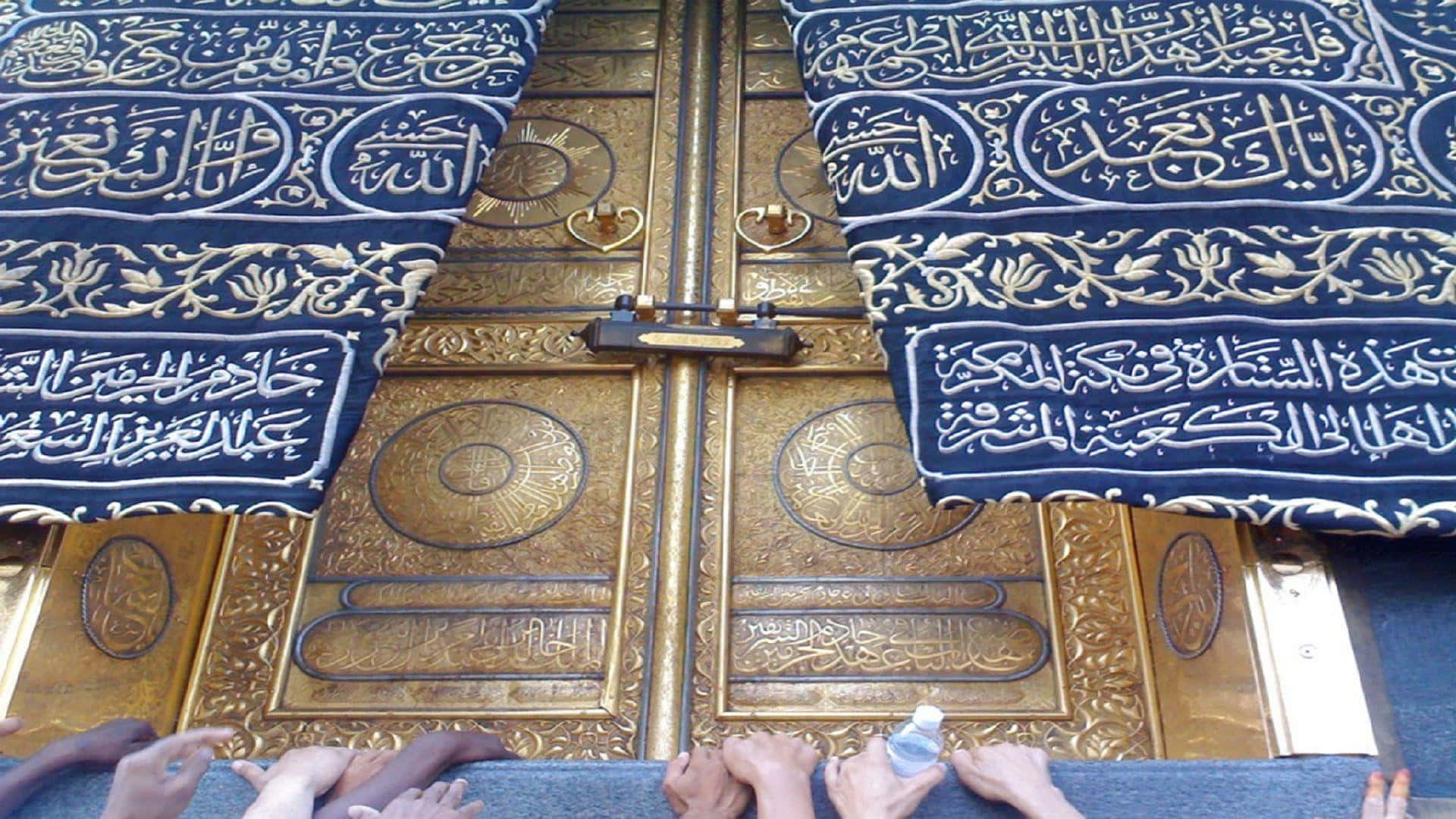 Kaaba 桌布 壁紙 — 金色華麗的門上飾有複雜的阿拉伯書法，覆蓋著藍色布料，雙手向上觸摸它們。