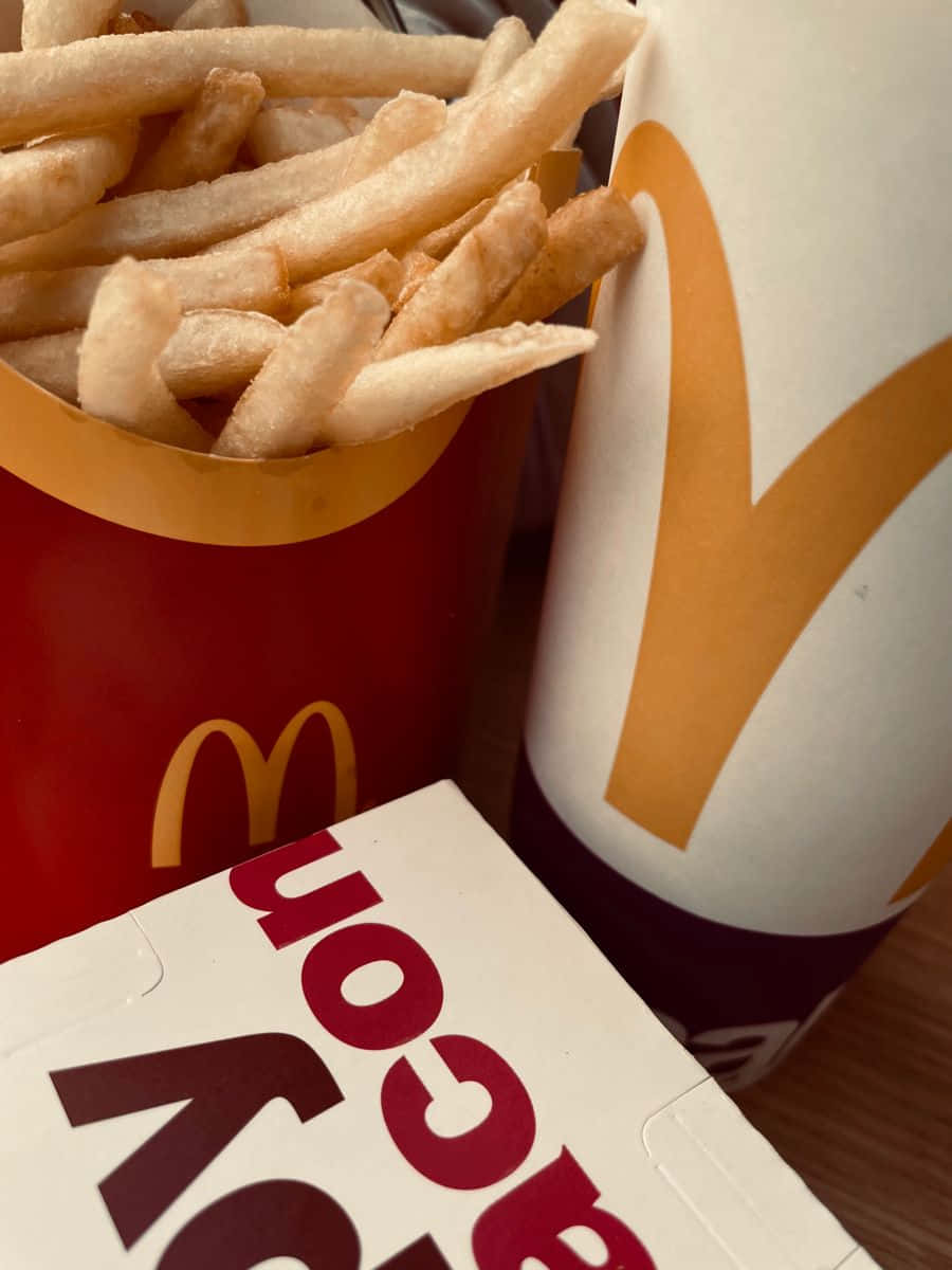 drinks 桌布 壁紙 — 金色薯條從紅色麥當勞杯中溢出，旁邊有飲料杯和培根盒放在木桌上。