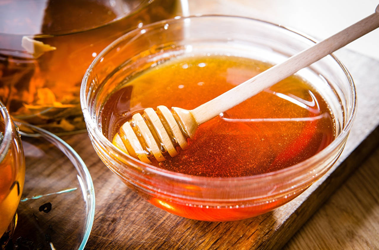 Honeycomb 桌布 壁紙 — 金色蜂蜜在玻璃碗中閃閃發光，內有木製蘸勺，置於質樸的木質表面上。