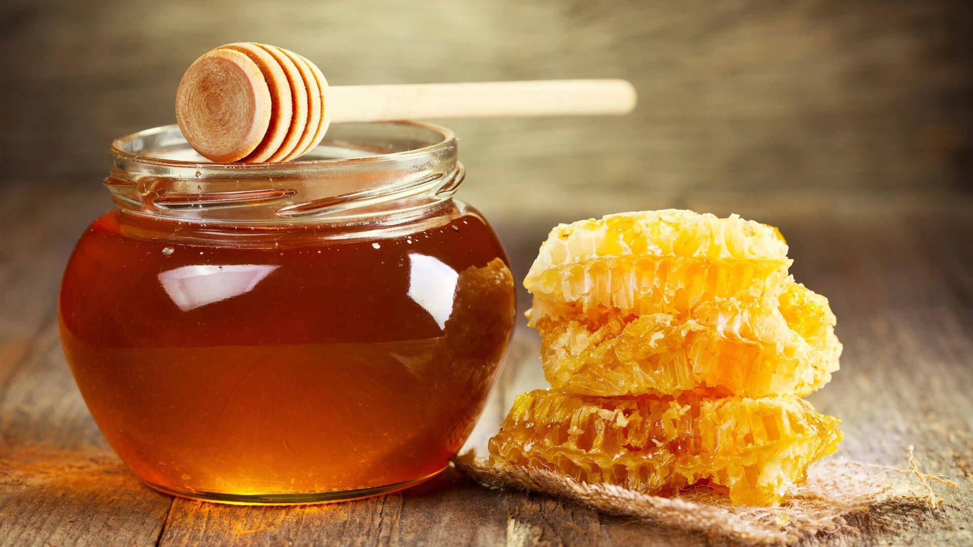 honey 桌布 壁紙 — 金色蜂蜜在玻璃罐中閃閃發光，旁邊堆疊的蜂巢放在質樸的木桌上。