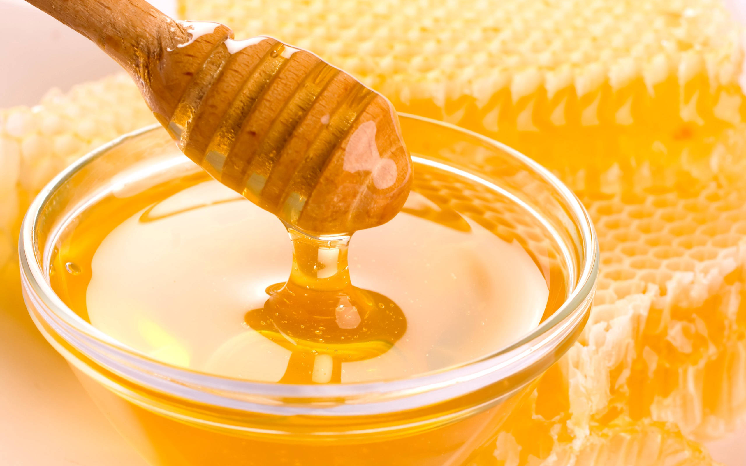 honey 桌布 壁紙 — 金色蜂蜜從木勺滴入玻璃碗中，旁邊有蜂巢。
