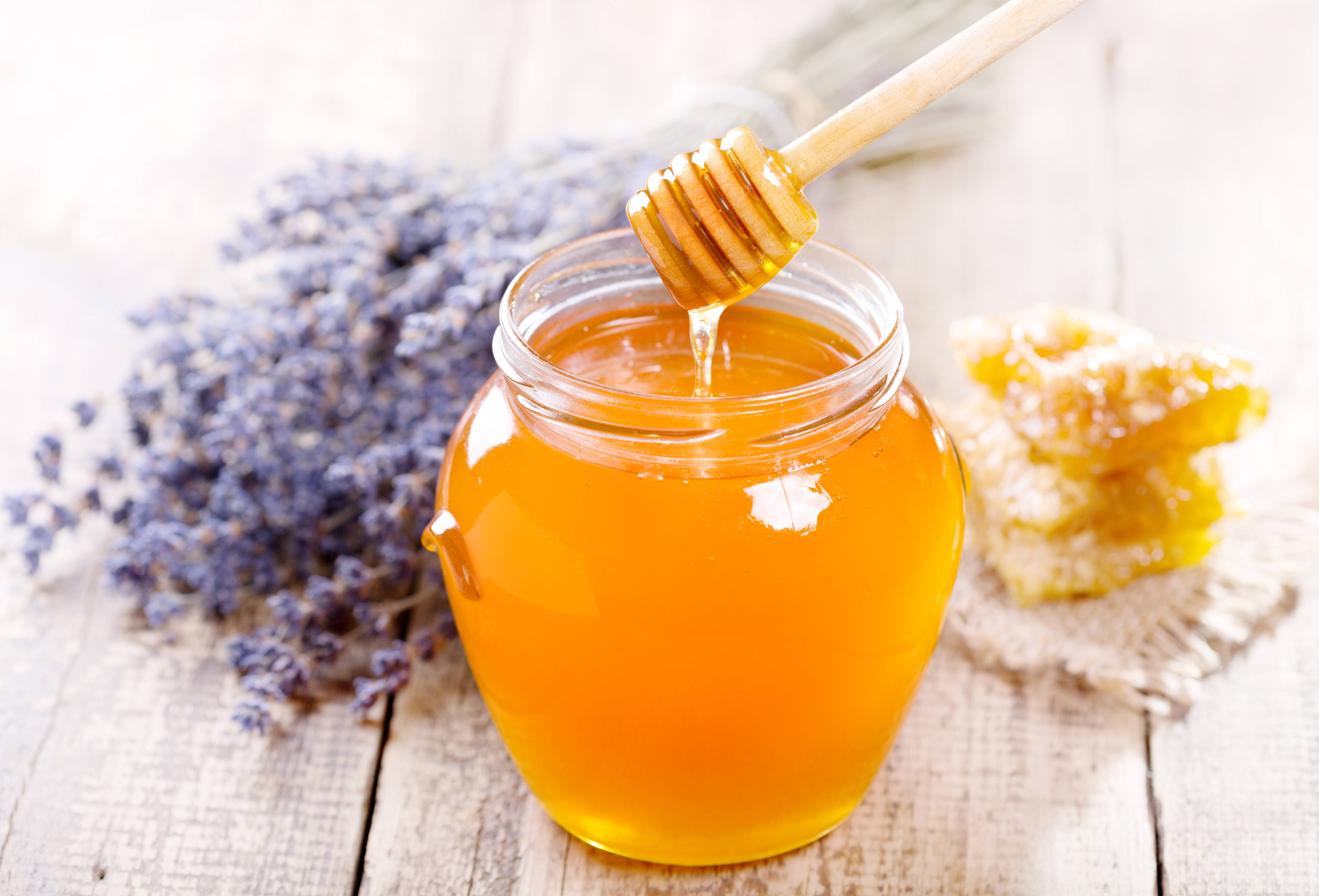 honey 桌布 壁紙 — 金色蜂蜜從木勺滴入玻璃罐中，旁邊有薰衣草和蜂巢在質樸的木桌上。