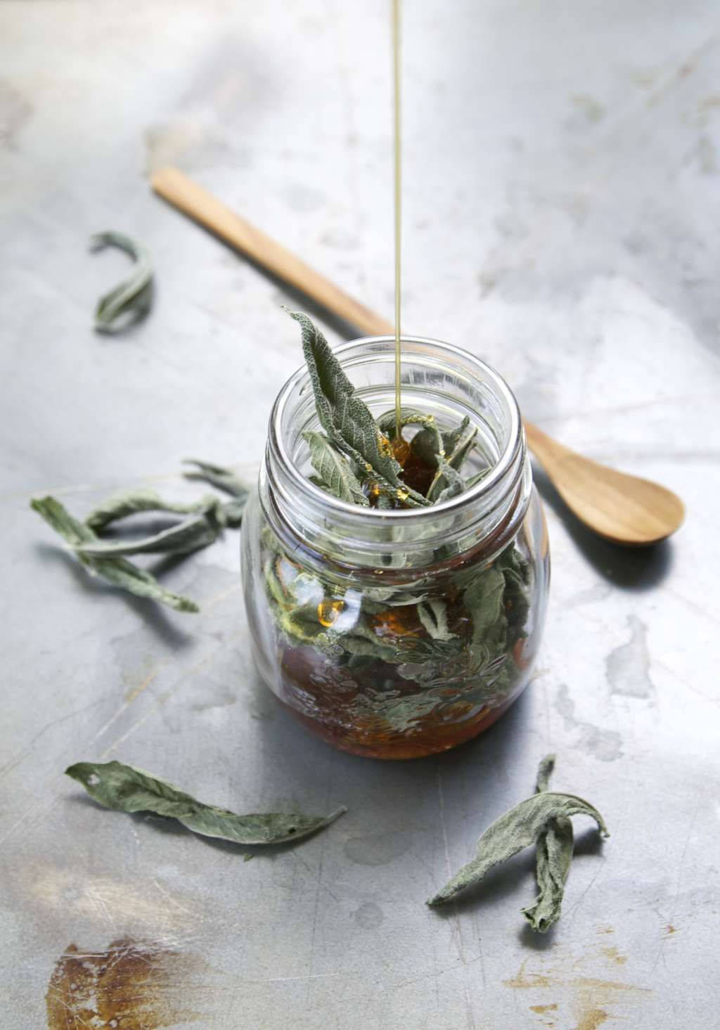 Green Leaves 桌布 壁紙 — 金色蜂蜜滴入裝滿乾燥鼠尾草葉的玻璃罐中，置於質樸的金屬表面上。