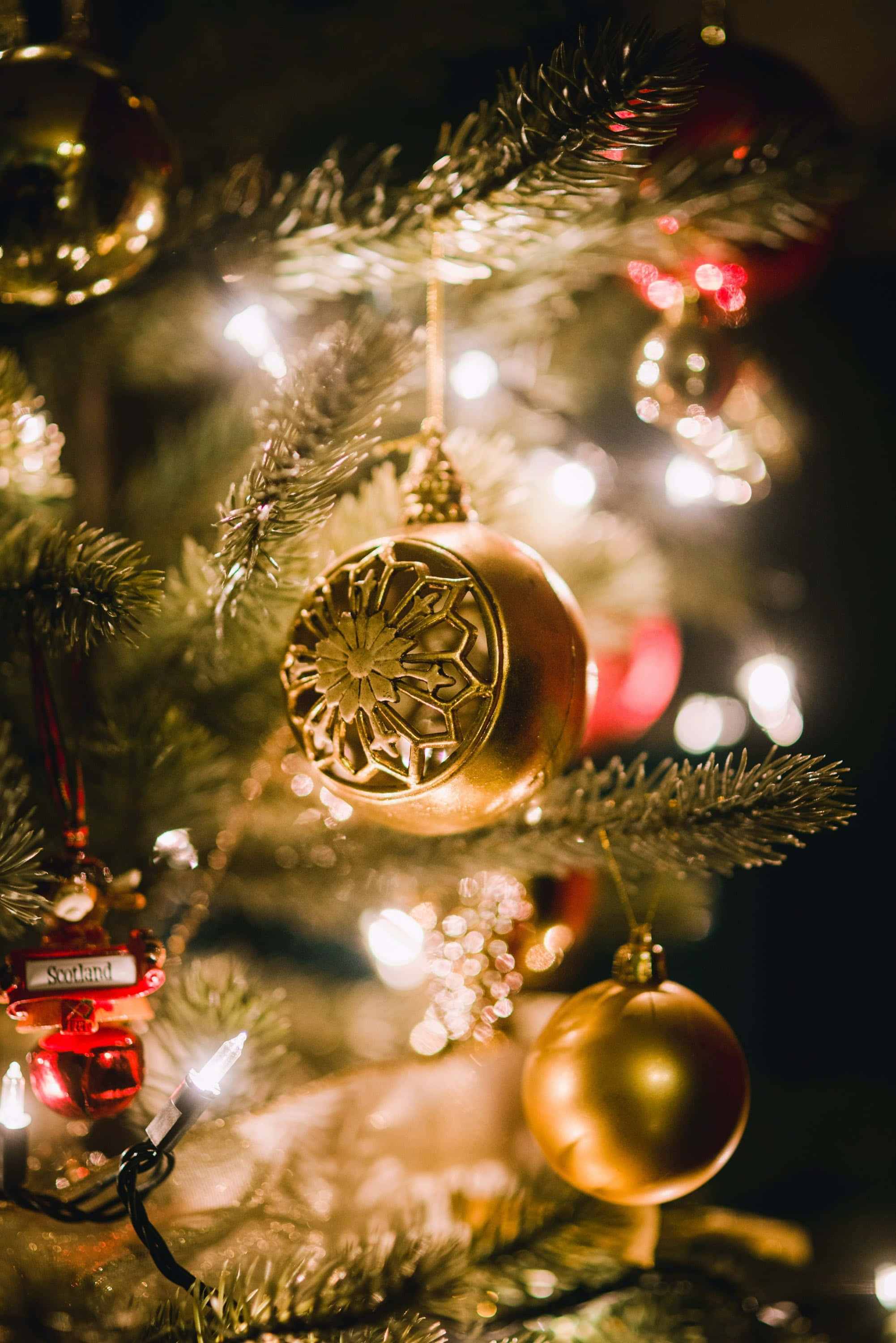Gold Christmas 桌布 壁紙 — 金色裝飾和閃爍燈光在聖誕樹上的特寫，背景柔和散景。