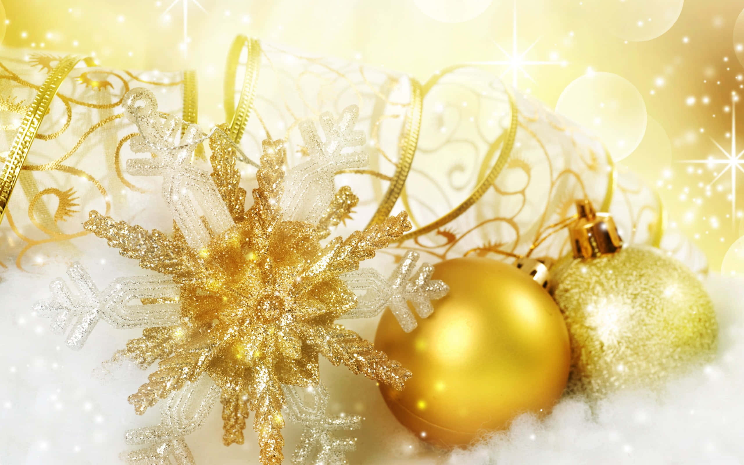 Gold Christmas 桌布 壁紙 — 金色裝飾品和閃閃發光的雪花躺在蓬鬆的雪地上，背景是燦爛的金色散景。