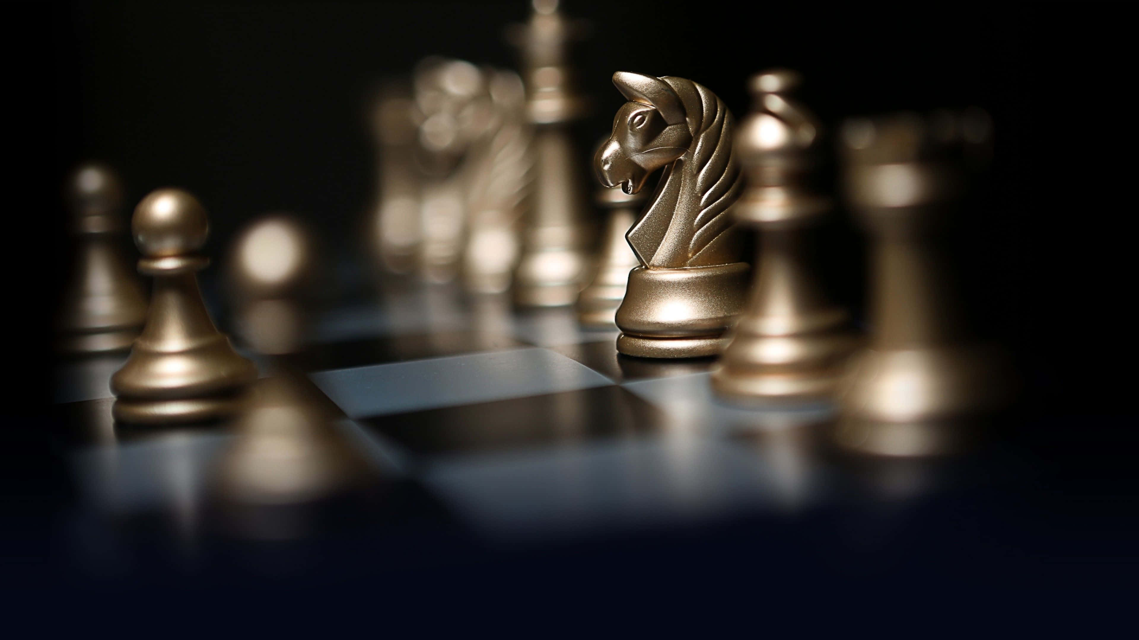 西洋棋 桌布 壁紙 — 金色西洋棋棋子在戲劇性燈光下於深色棋盤上閃耀，淺景深突顯前景的騎士。