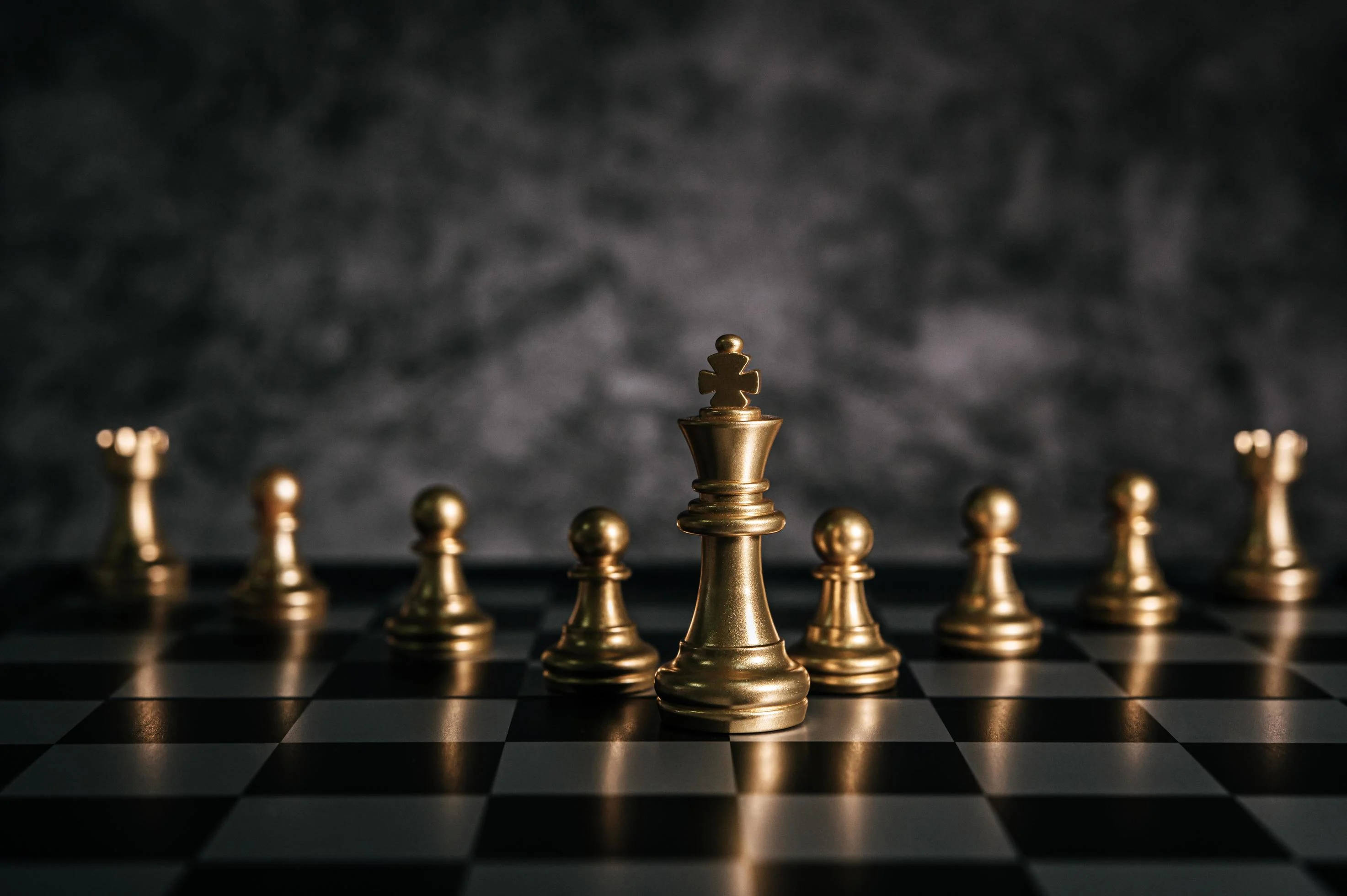西洋棋 桌布 壁紙 — 金色西洋棋棋子擺放在棋盤上，背景是煙霧瀰漫的黑暗環境，帶有戲劇性的燈光效果。