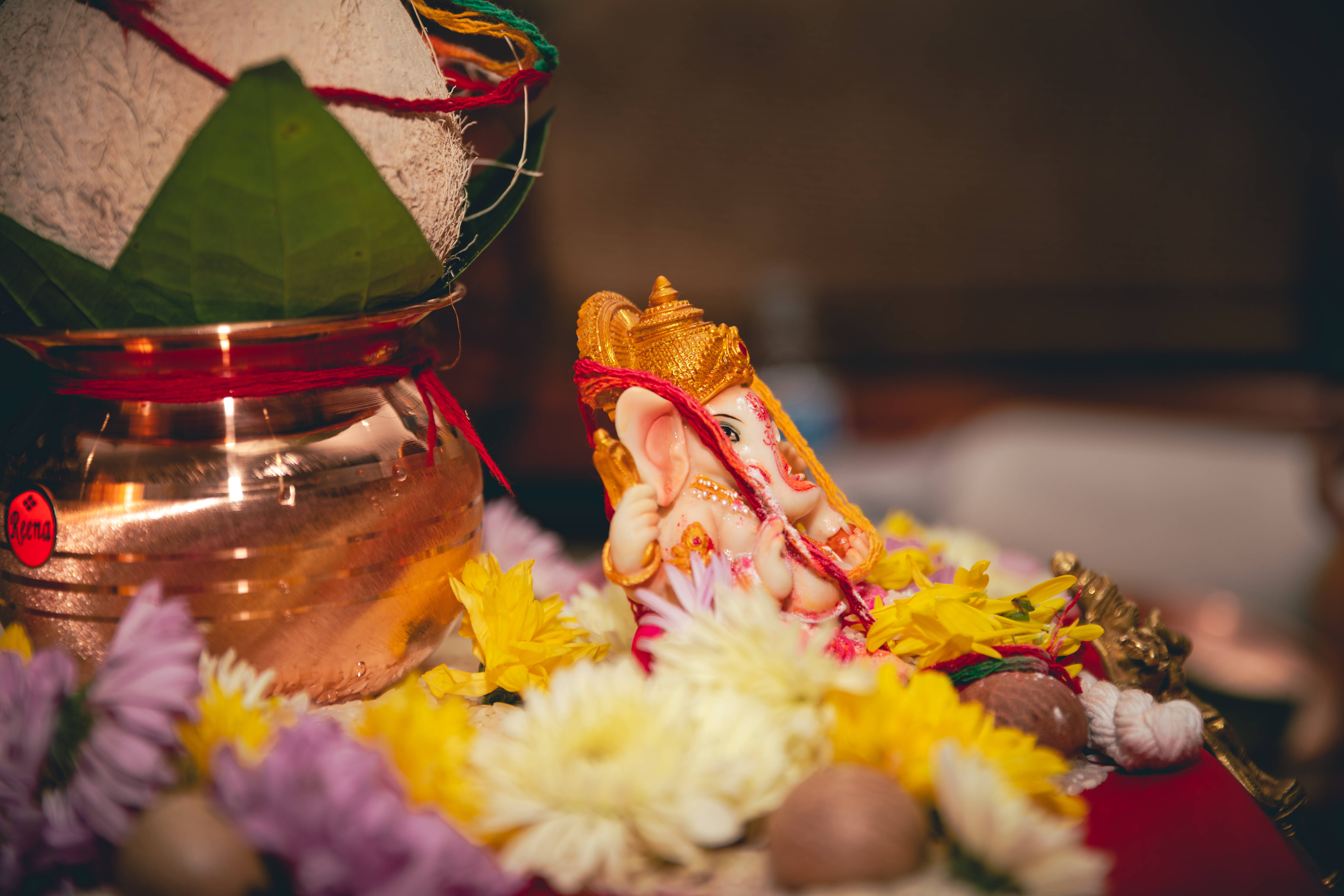 Bappa 桌布 壁紙 — 金色象神像被色彩繽紛的花朵和一個裝有椰子及樹葉供品的銅器所環繞。