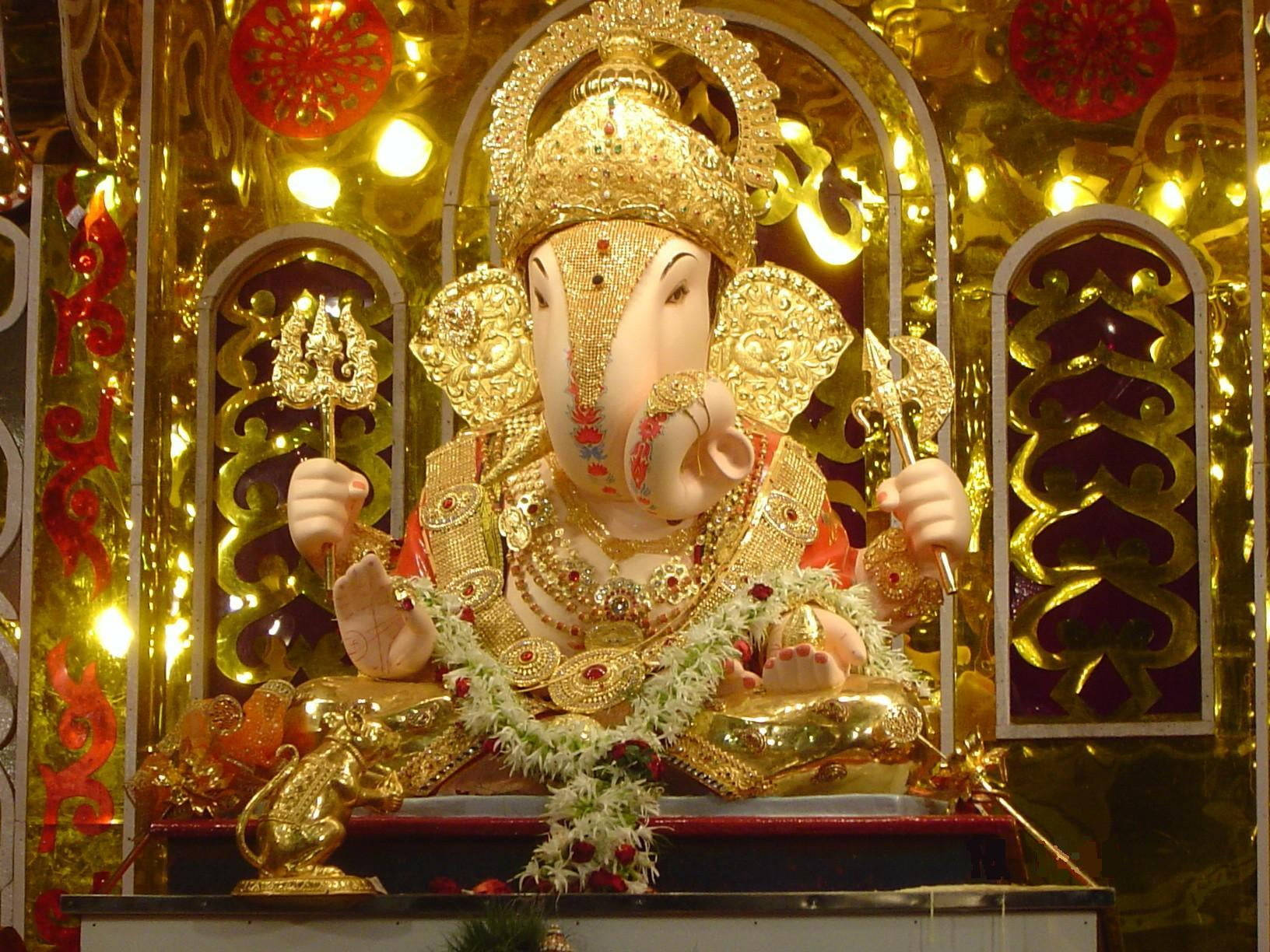 Ganesh 桌布 壁紙 — 金色象神像飾以珠寶和鮮花，莊嚴地坐在由溫暖燈光照亮的閃閃發光的神龕中。