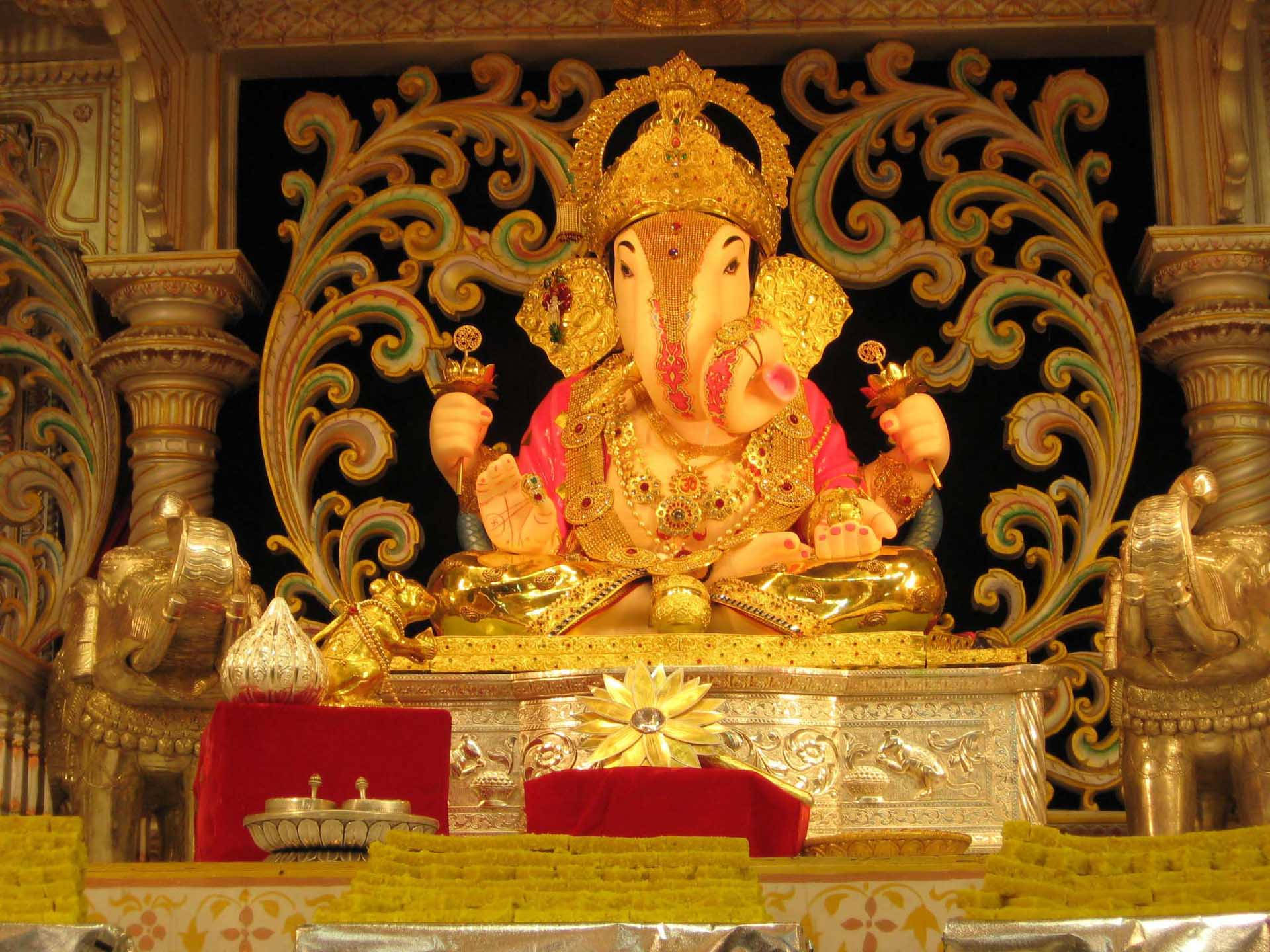ganpati HD 桌布 壁紙 — 金色象神像飾有珠寶，莊嚴地坐在華麗的寶座上，周圍環繞著精緻的雕刻和供品。