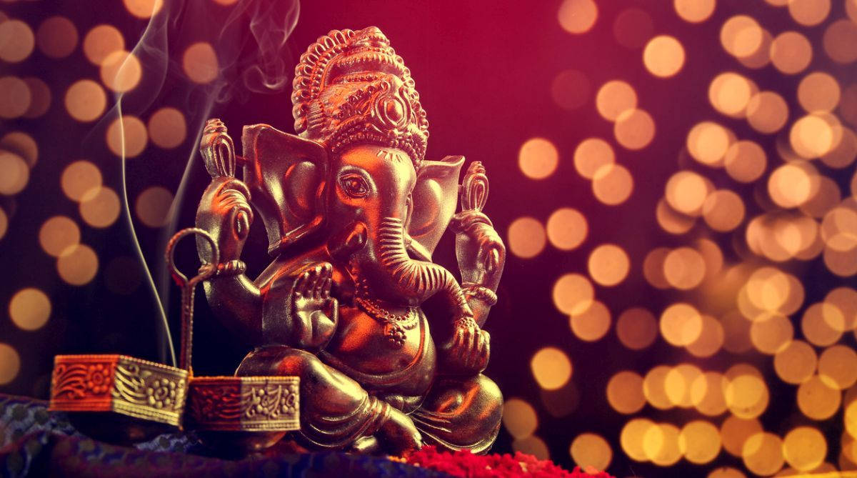 ganpati HD 桌布 壁紙 — 金色象神雕像，旁邊有煙霧升起，背景是溫暖的散景和發光的燈光。