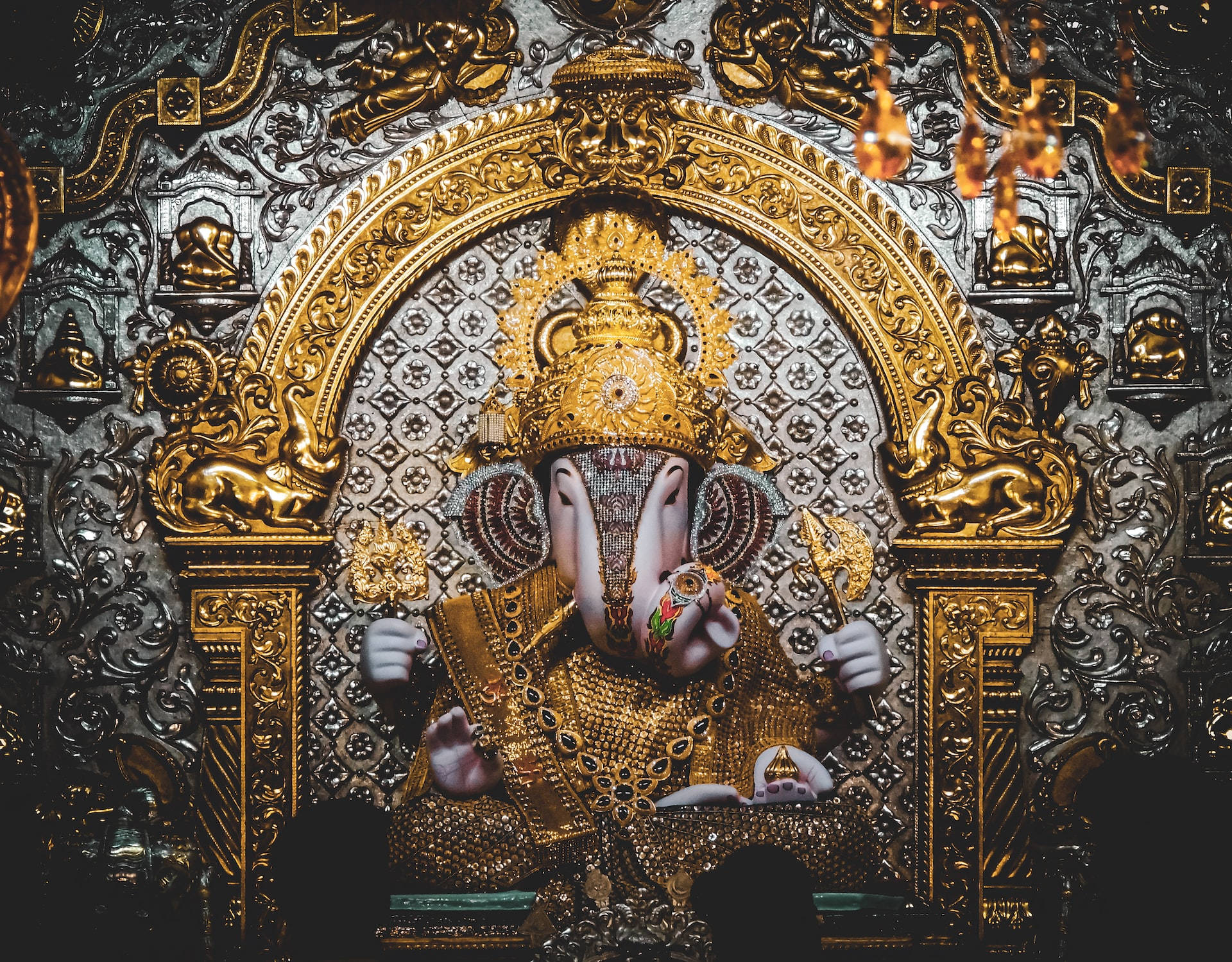 statue 桌布 壁紙 — 金色象神雕像莊嚴地坐在裝飾華麗的寶座上，寶座上有精緻的雕刻和懸掛的燈籠。