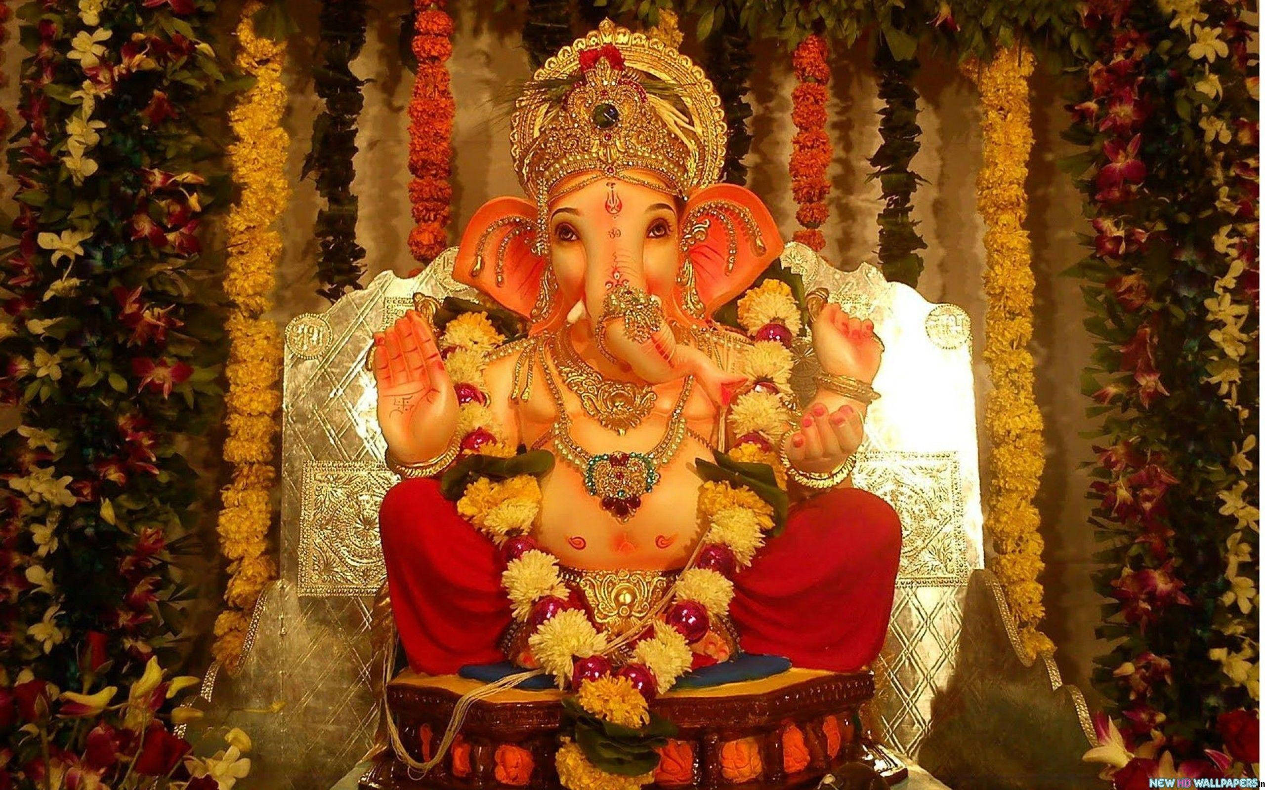 ganpati HD 桌布 壁紙 — 金色象神雕像飾以紅黃花朵，端莊地坐在華麗寶座上，上方掛滿節日花環。
