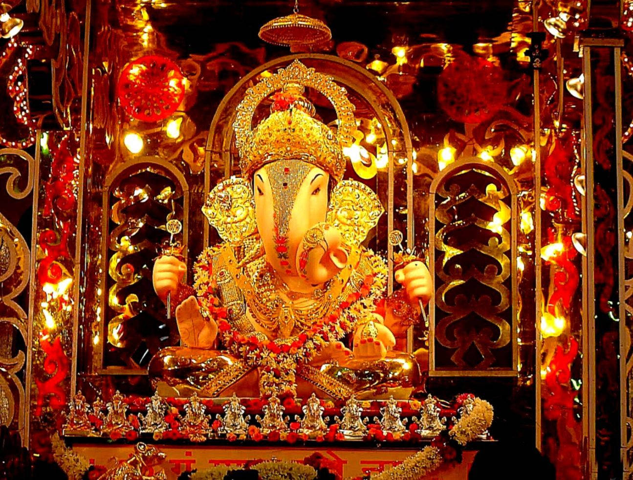 ganpati HD 桌布 壁紙 — 金色象神雕像飾有珠寶和紅花，莊嚴地坐在一個閃閃發光的神龕中，被溫暖的燈光照亮。