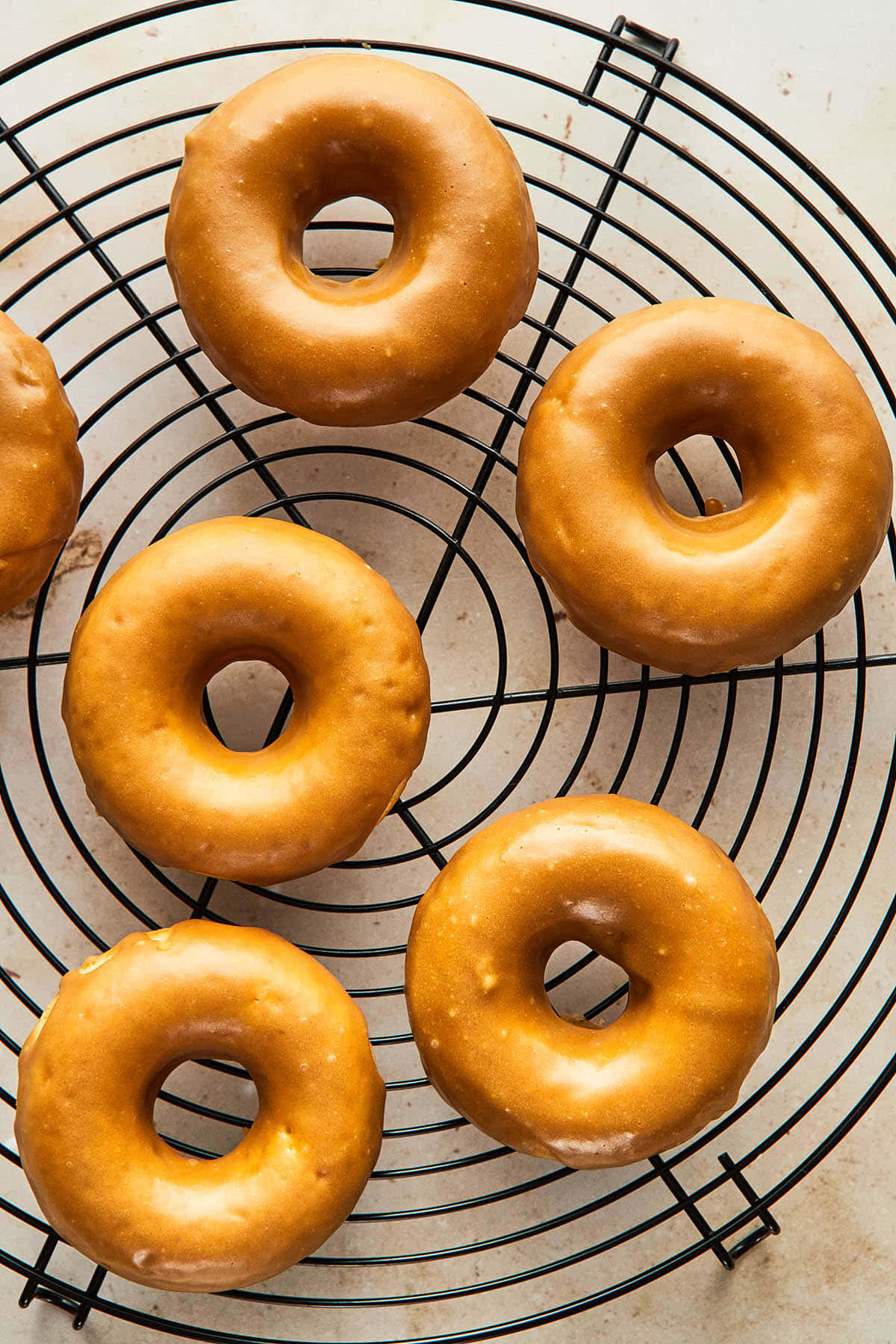 Glazed Donut 桌布 壁紙 — 金色釉面甜甜圈放在淺色檯面上的黑色金屬冷卻架上。