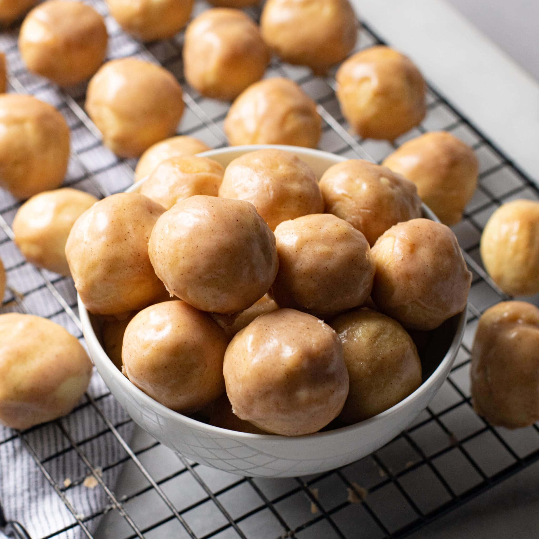 Glazed Donut 桌布 壁紙 — 金色釉面甜甜圈球堆在白色碗中，放在冷卻架上，周圍散落更多。