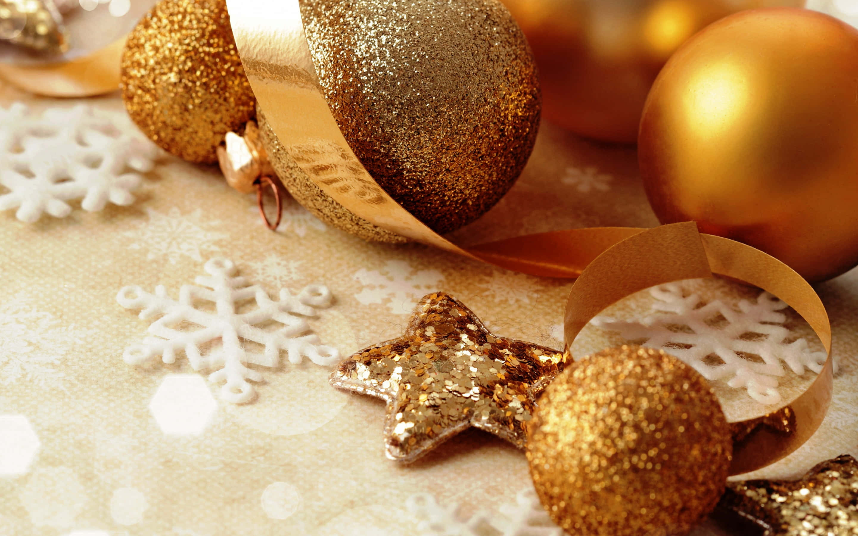 Gold Christmas 桌布 壁紙 — 金色閃亮裝飾品和白色雪花停留在閃爍的金色紋理表面上。