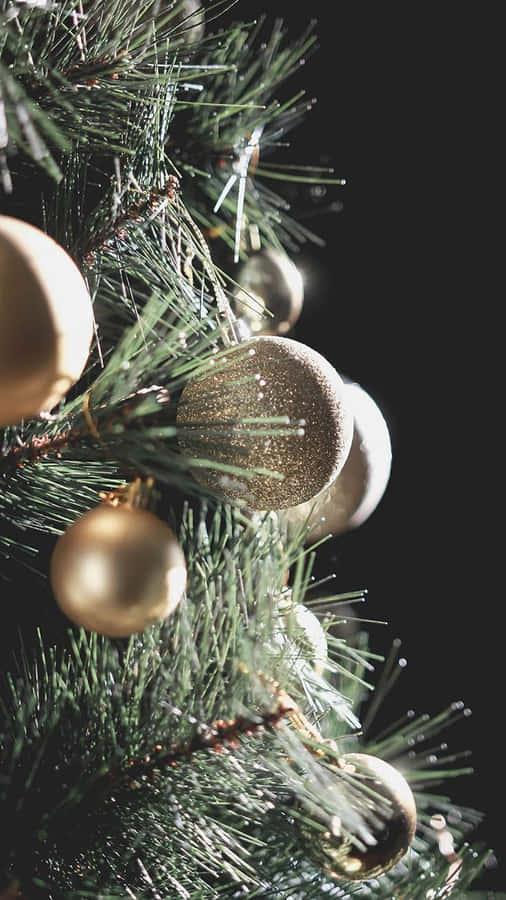 Aesthetic Christmas Tree 桌布 壁紙 — 金色閃粉和啞光裝飾品掛在深綠色松樹枝上，黑色背景的特寫。