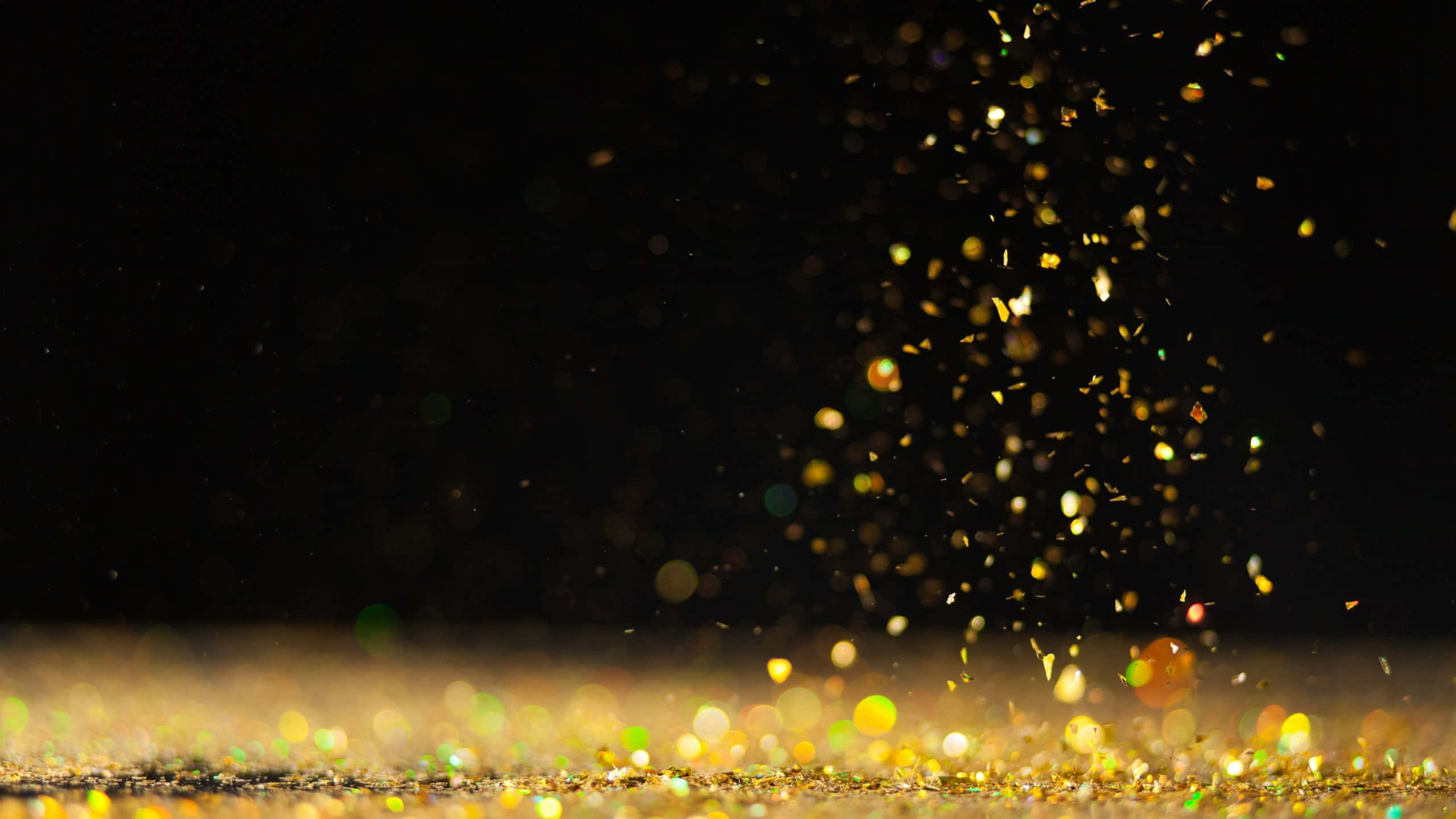Black And Gold Glitter 桌布 壁紙 — 金色閃粉粒子在深黑色背景上爆裂移動，營造出閃爍的節日效果。