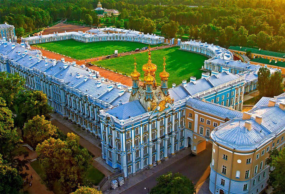 Catherine Palace 壁紙 — 金色陽光下，宏偉的藍金色彼得霍夫宮殿建築群被茂密的綠色花園和樹木環繞的鳥瞰圖。