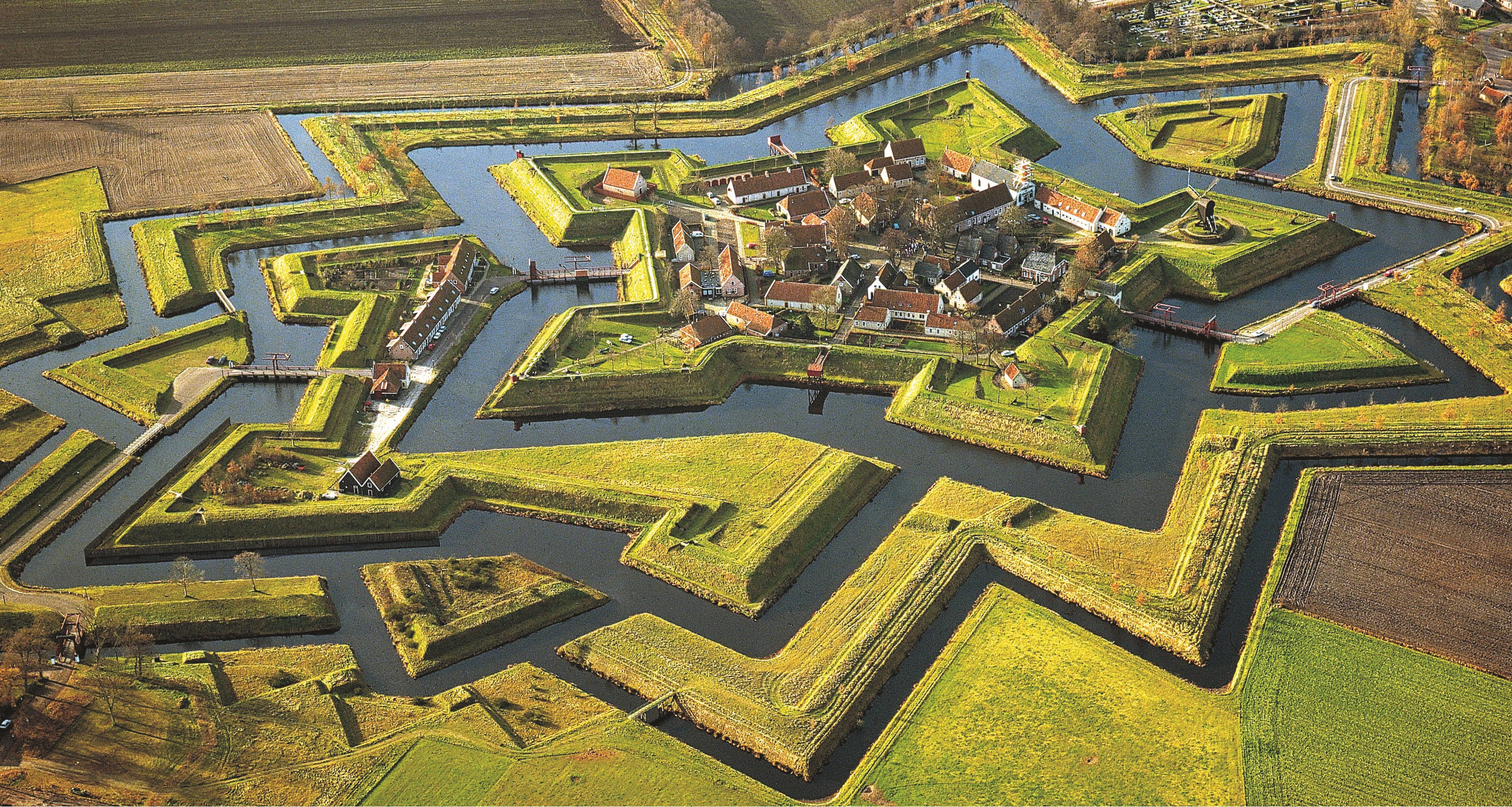 Netherlands 桌布 壁紙 — 金色陽光下，護城河和綠色田野環繞的星形堡壘鳥瞰圖。