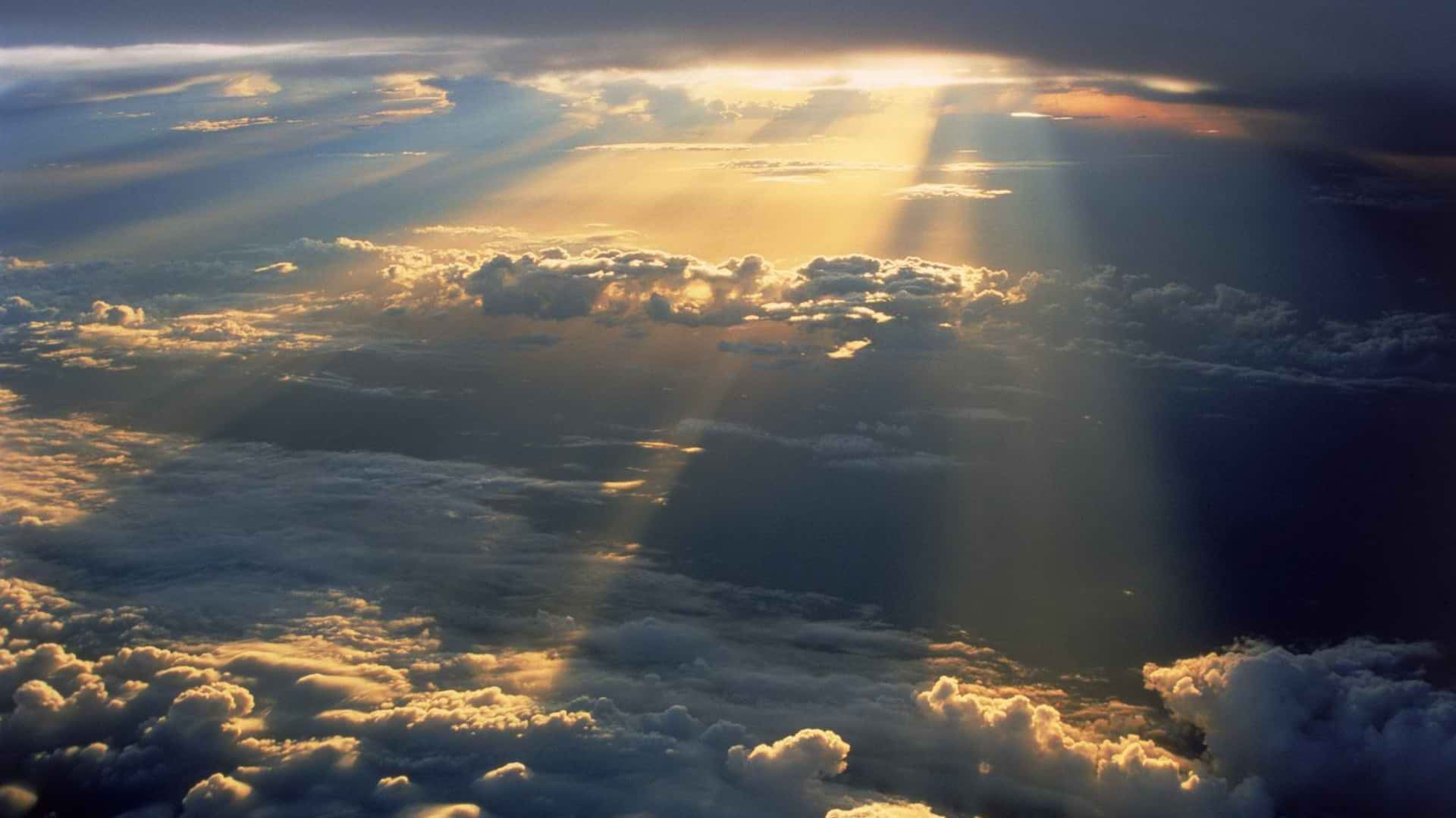 雲朵 桌布 壁紙 — 金色陽光從上方穿透戲劇性的雲層，照亮下方蓬鬆的白色和灰色雲層。