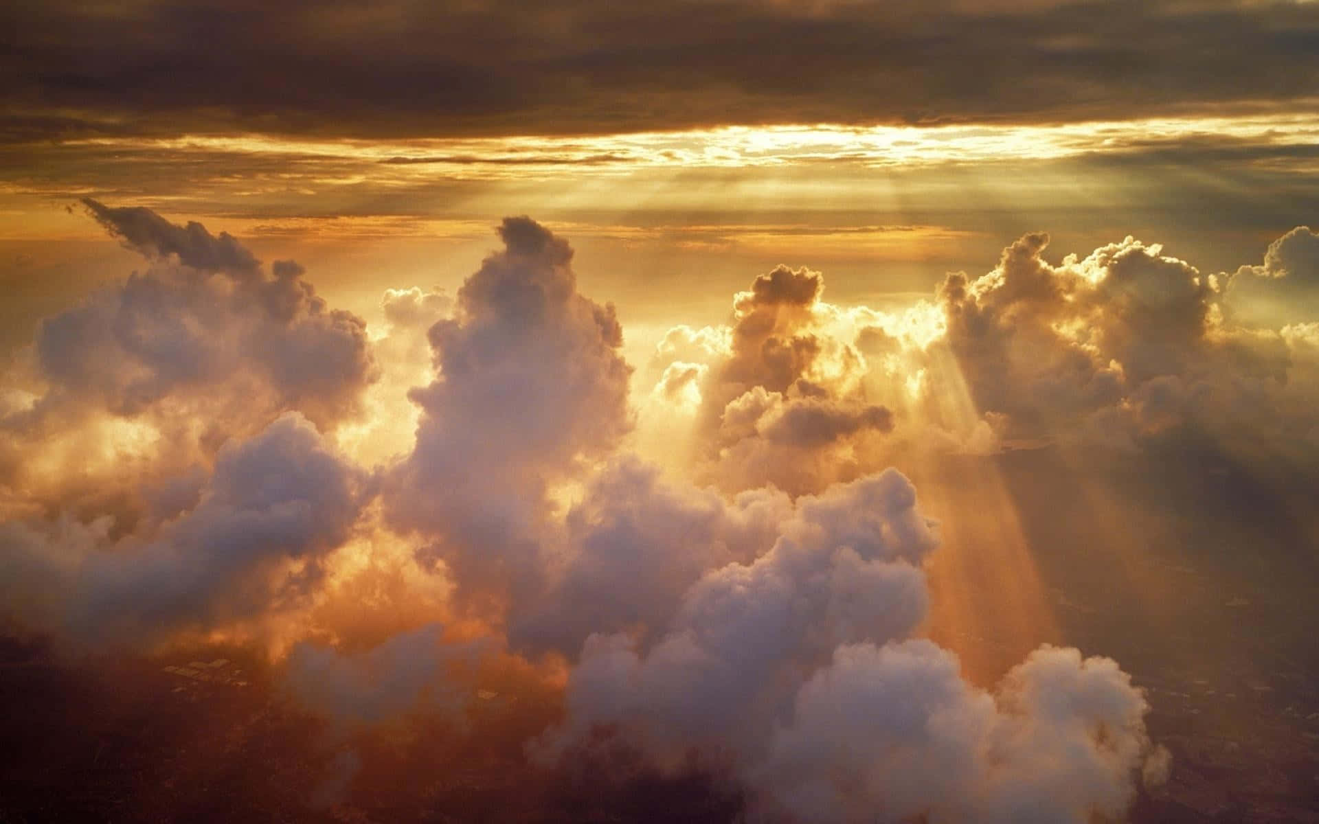 Heavenly 桌布 壁紙 — 金色陽光穿透高聳的雲層，呈現戲劇性的空中日落景觀。