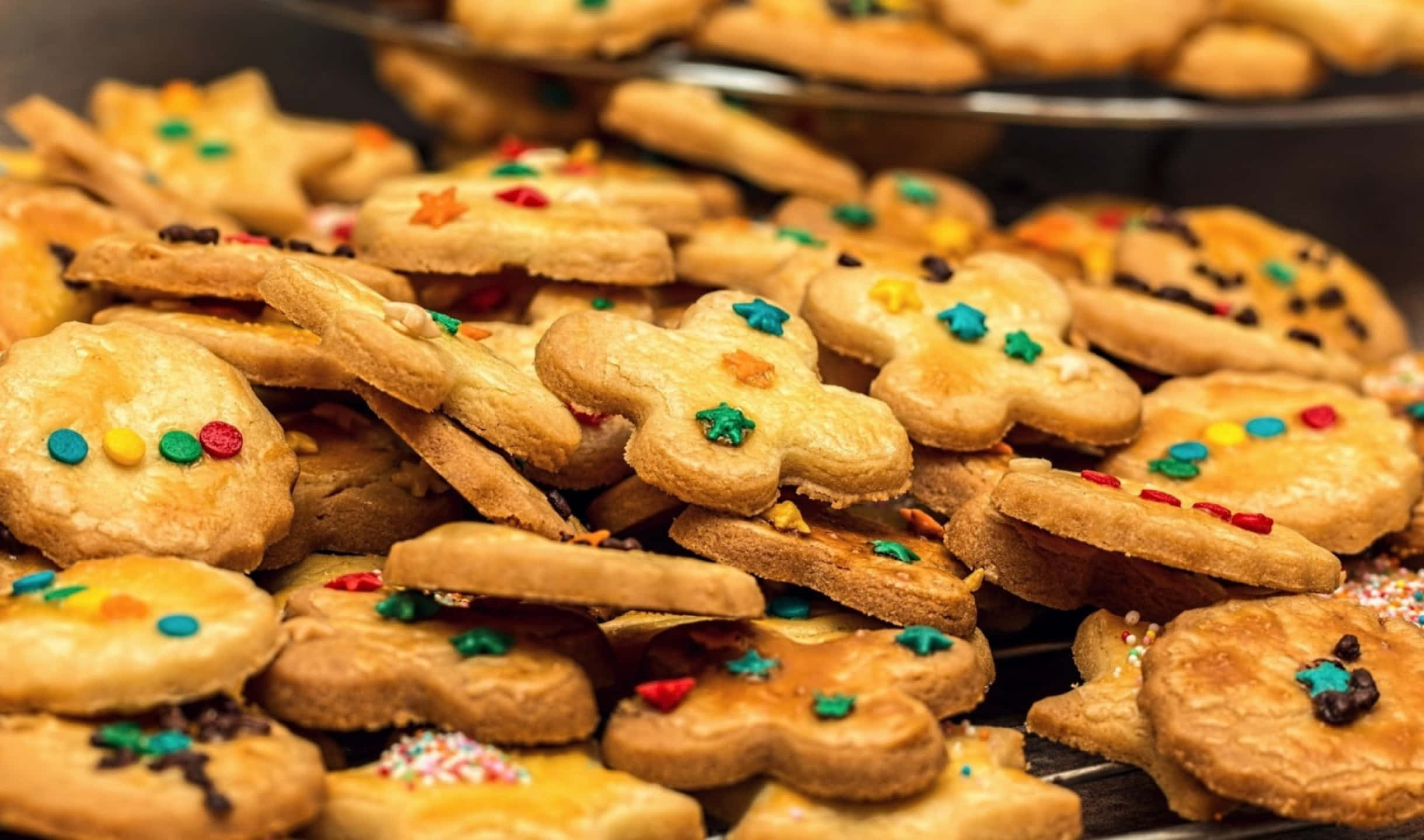 Cookies 桌布 壁紙 — 金色餅乾的特寫，形狀為星星和花朵，上面有彩色糖粒和巧克力豆。