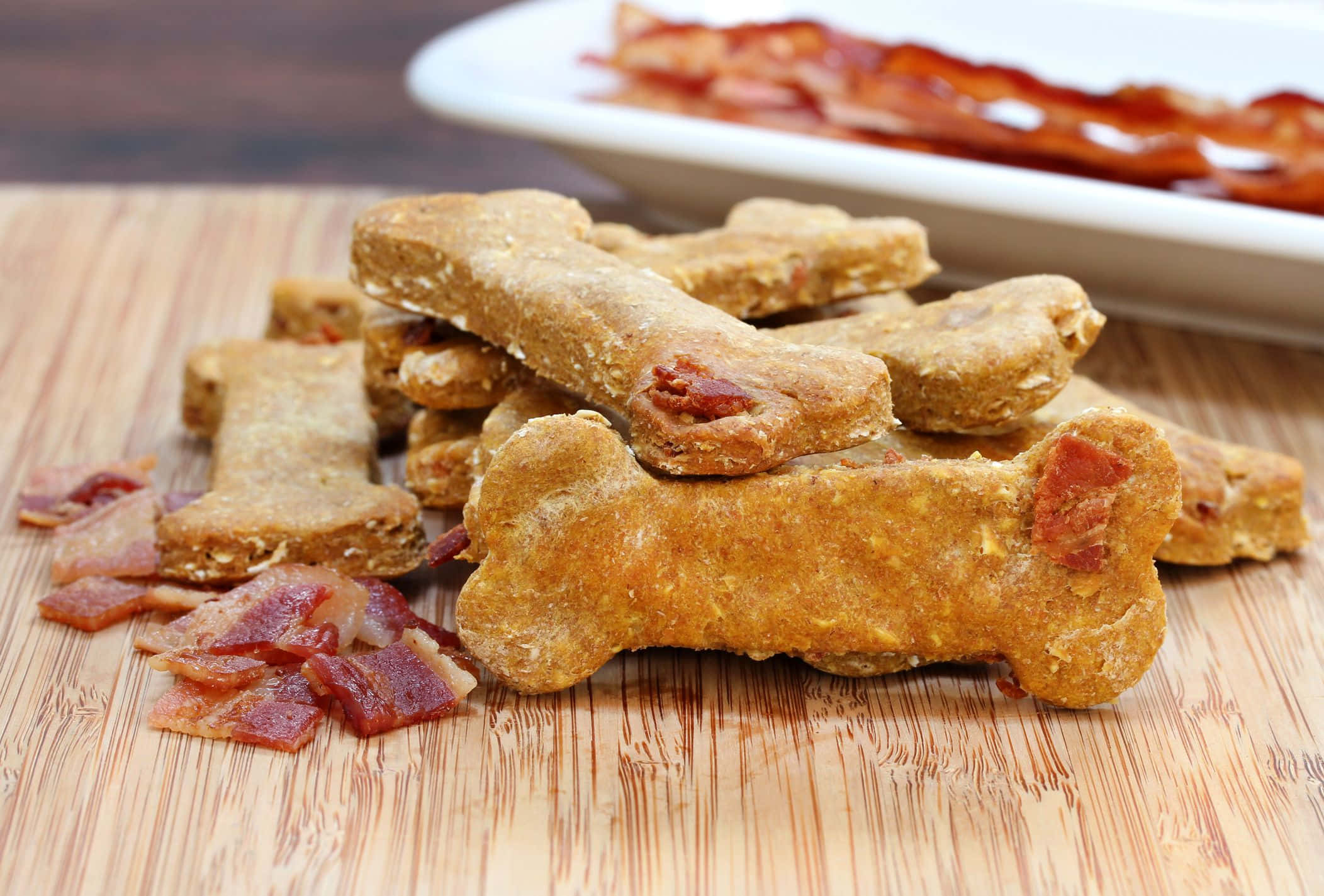 bacon 桌布 壁紙 — 金色骨形狗零食，上面鑲有培根粒，放在竹砧板上，背景有一碟培根。