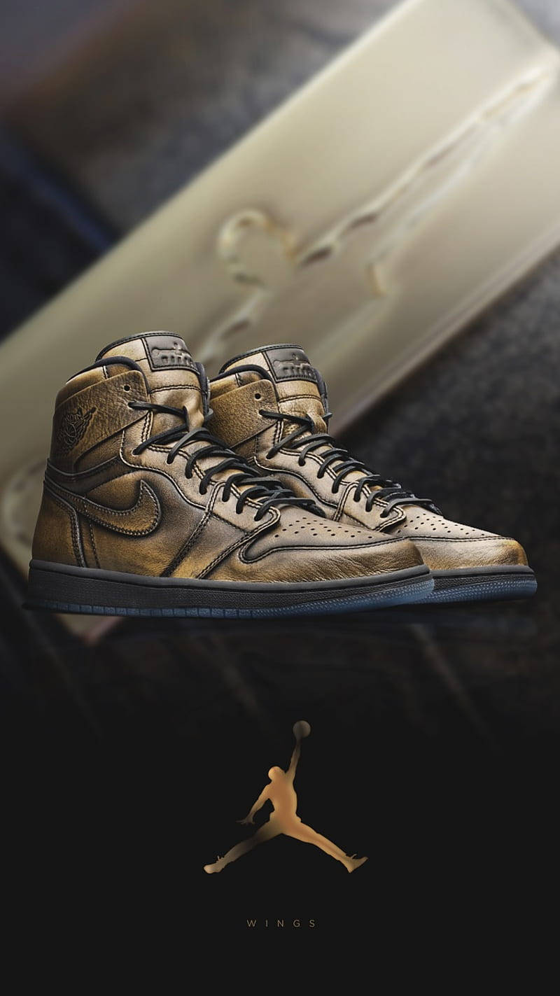 Nike Air Jordan 1 桌布 壁紙 — 金色高筒運動鞋搭配黑色鞋帶，放置在深色表面上，旁邊是一個帶有Jumpman標誌的金色盒子。