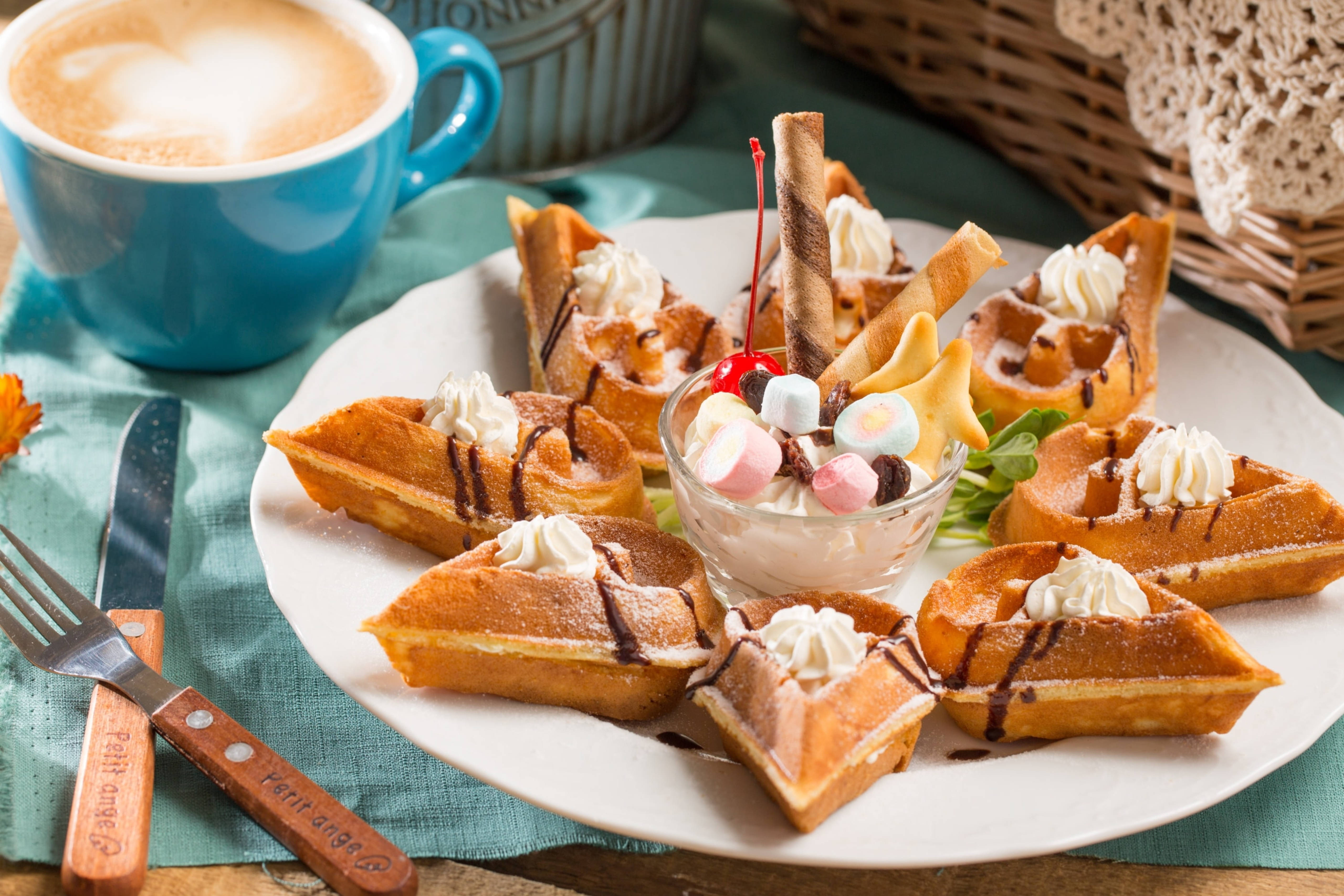 Waffle 桌布 壁紙 — 金色鬆餅三角形，上面有鮮奶油、巧克力醬和一個裝滿糖果的聖代，旁邊放著一個藍色咖啡杯，放在青綠色布上。