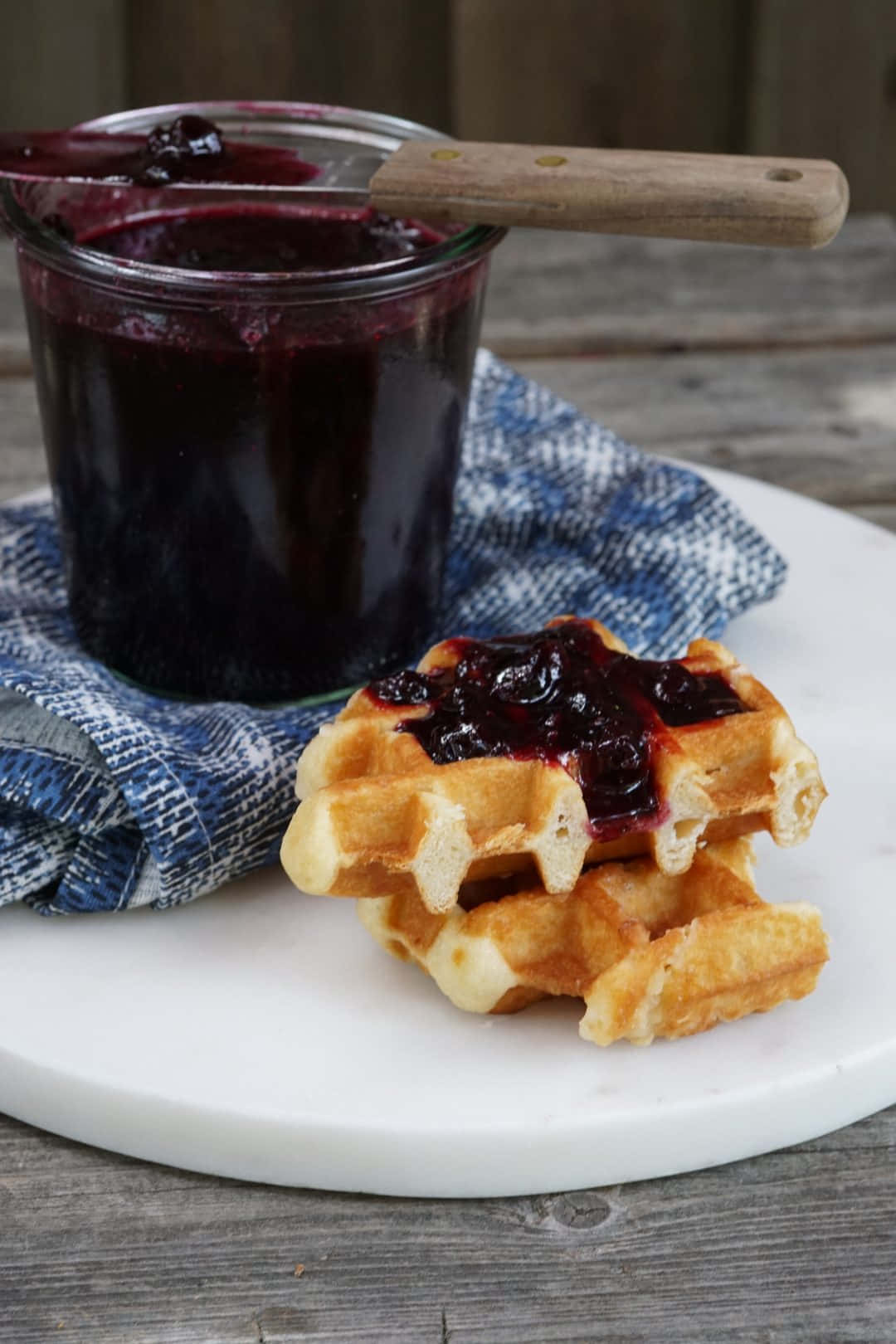 Blueberry Jam 桌布 壁紙 — 金色鬆餅堆疊搭配深色莓果醬，旁邊有玻璃罐，放在大理石盤上，鋪有藍色布。