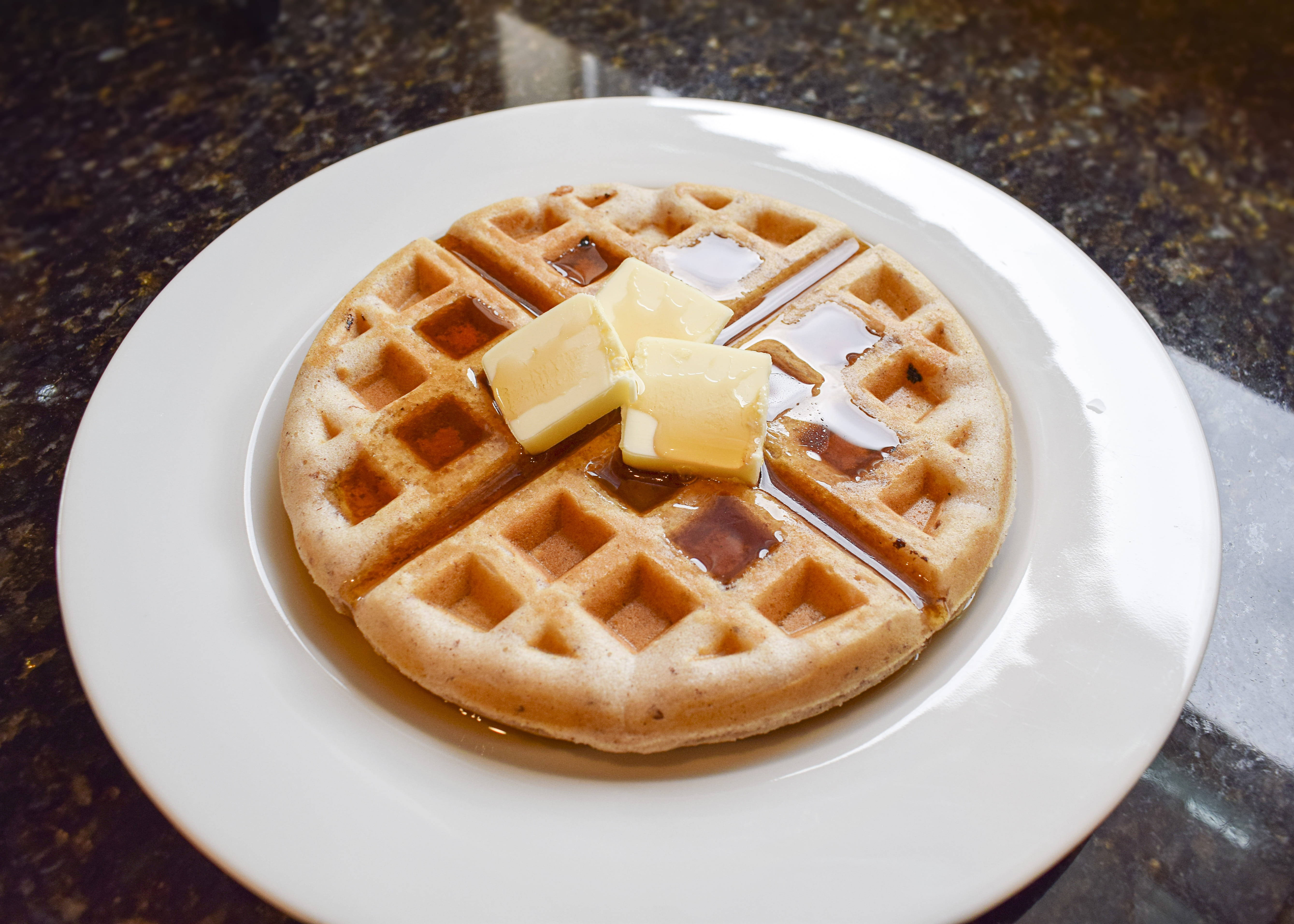 Waffle 桌布 壁紙 — 金色鬆餅放在白色盤子上，配上融化奶油和糖漿，置於深色花崗岩檯面上。