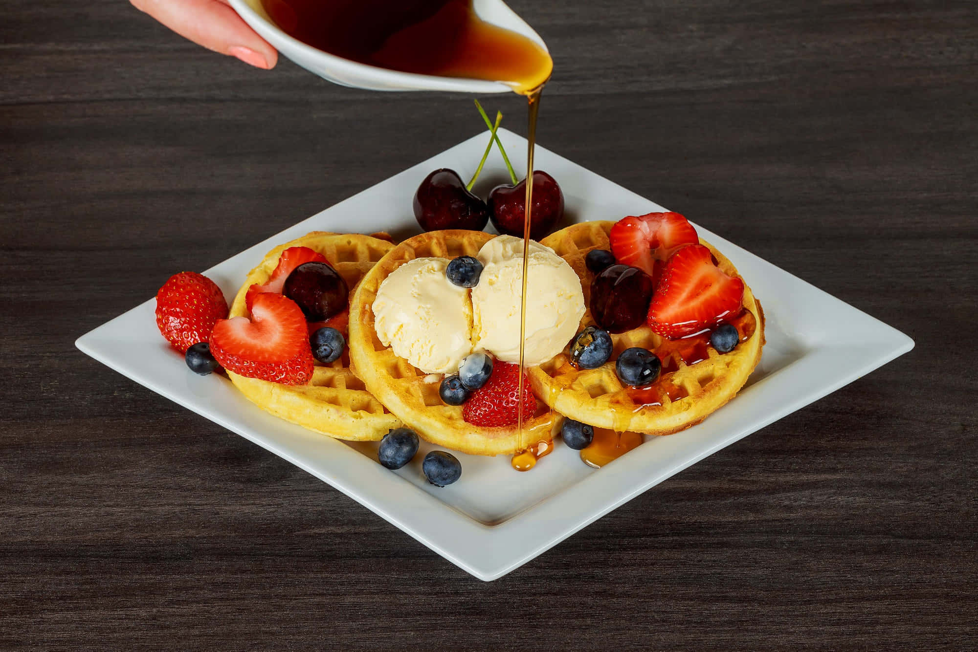 Waffle 桌布 壁紙 — 金色鬆餅配上冰淇淋、新鮮莓果，並從白色壺中倒出糖漿在深色木桌上。