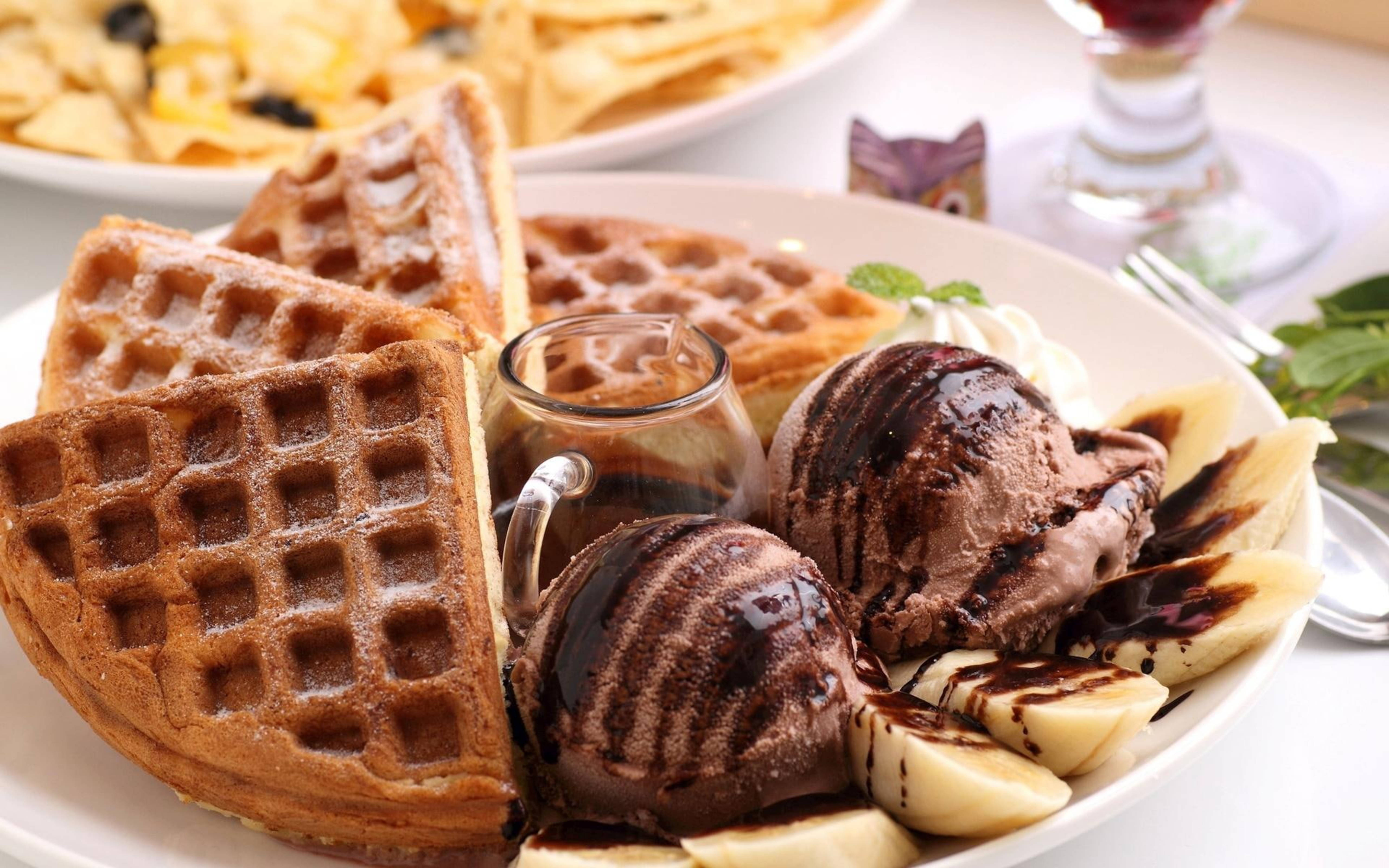 Waffle 桌布 壁紙 — 金色鬆餅配上巧克力冰淇淋、香蕉片和糖漿，放在白色盤子上。