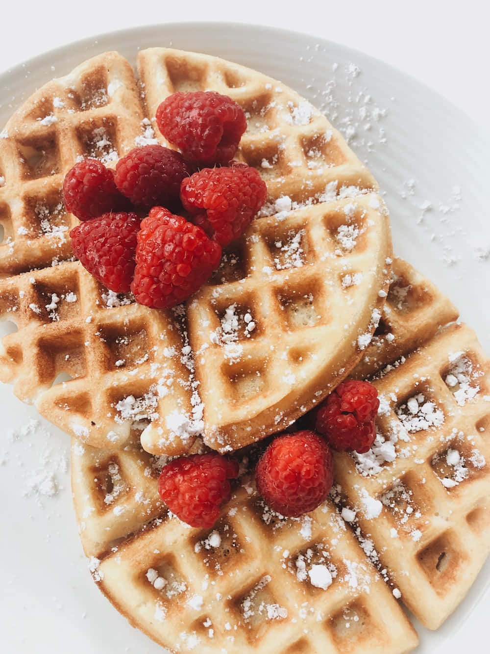 Waffle 桌布 壁紙 — 金色鬆餅配上新鮮覆盆子和糖粉，放在白色盤子上。