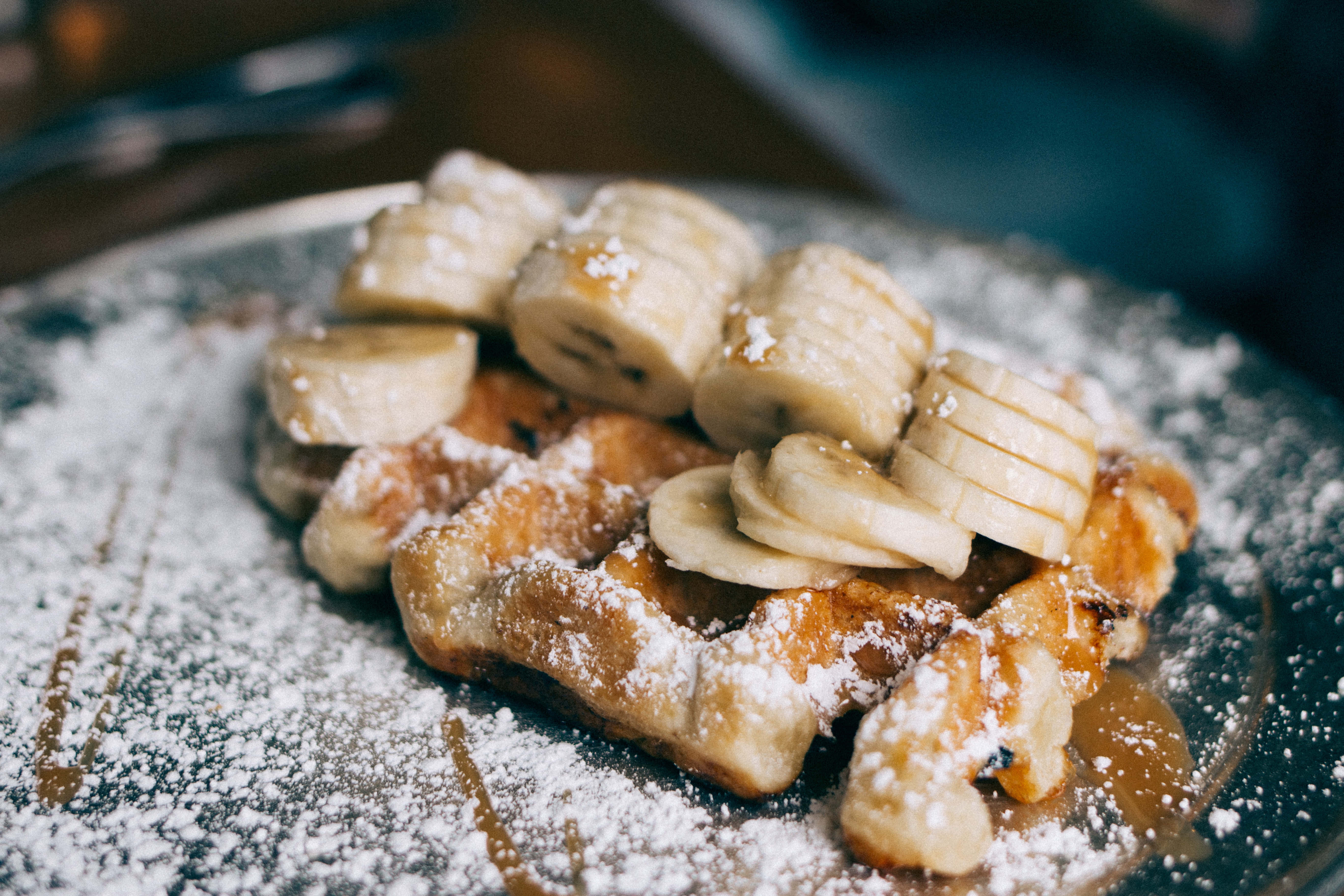 Waffle 桌布 壁紙 — 金色鬆餅配上香蕉片、糖粉和糖漿，放在深色盤子上。