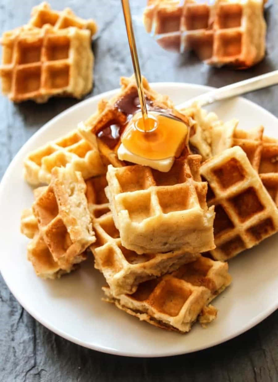 Waffle 桌布 壁紙 — 金色鬆餅高高疊在白色盤子上，蜂蜜滴在奶油上的特寫鏡頭。