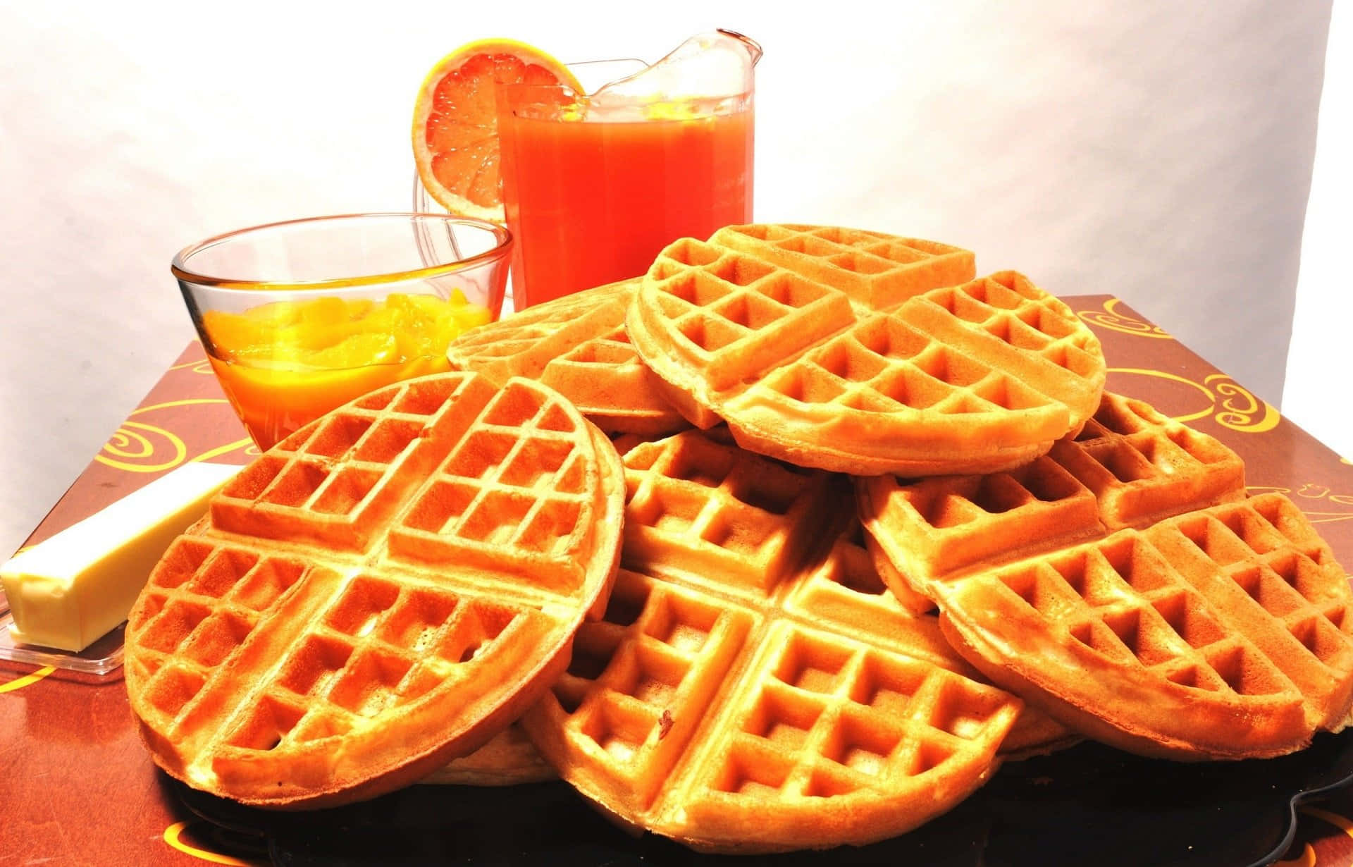 Waffle 桌布 壁紙 — 金色鬆餅高高疊起，配上一杯柳橙汁和奶油，放在有圖案的托盤上。