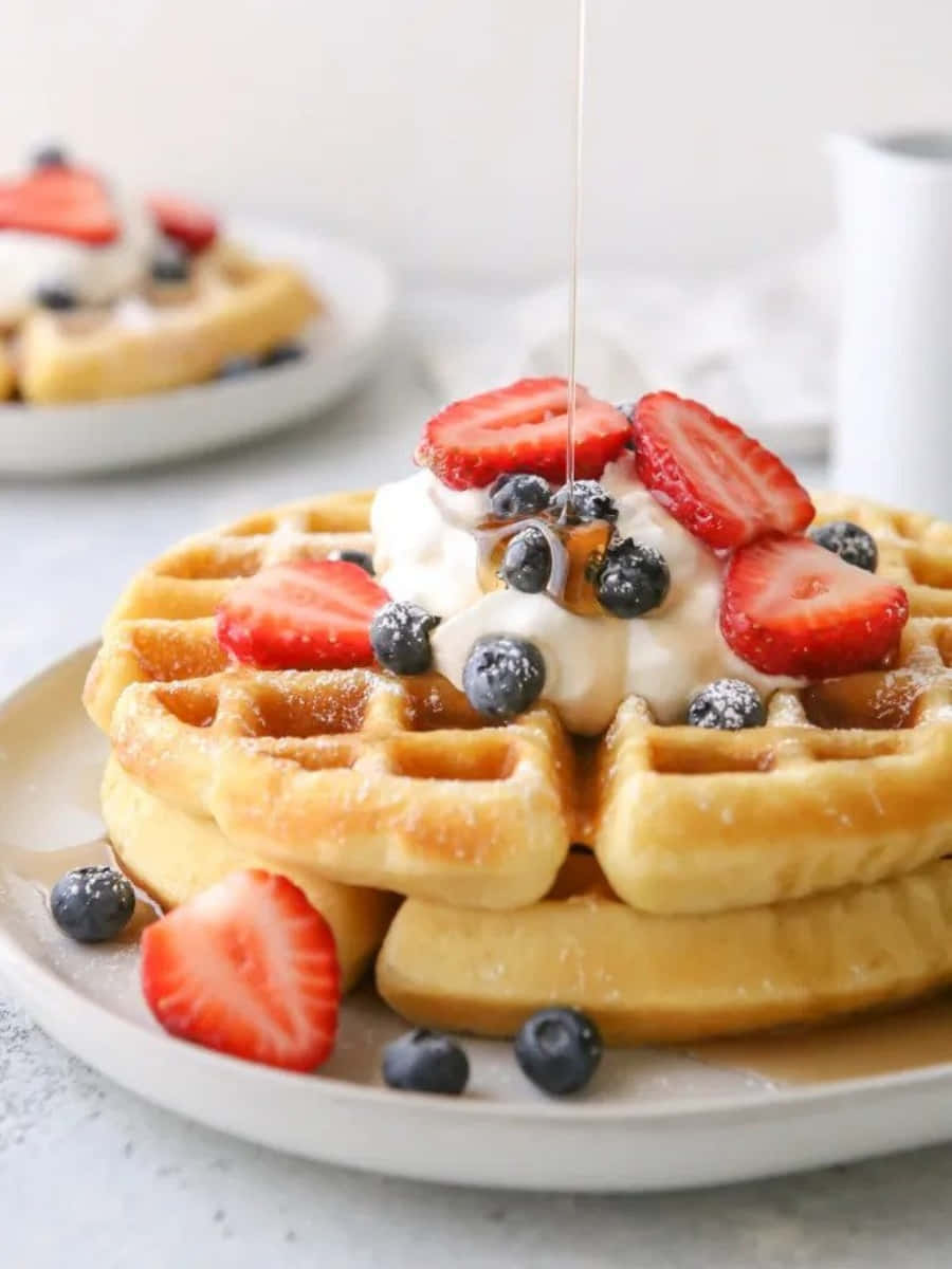 Waffle 桌布 壁紙 — 金色鬆餅高高疊起，配上新鮮草莓、藍莓和鮮奶油，糖漿滴落，營造甜蜜的早餐場景。