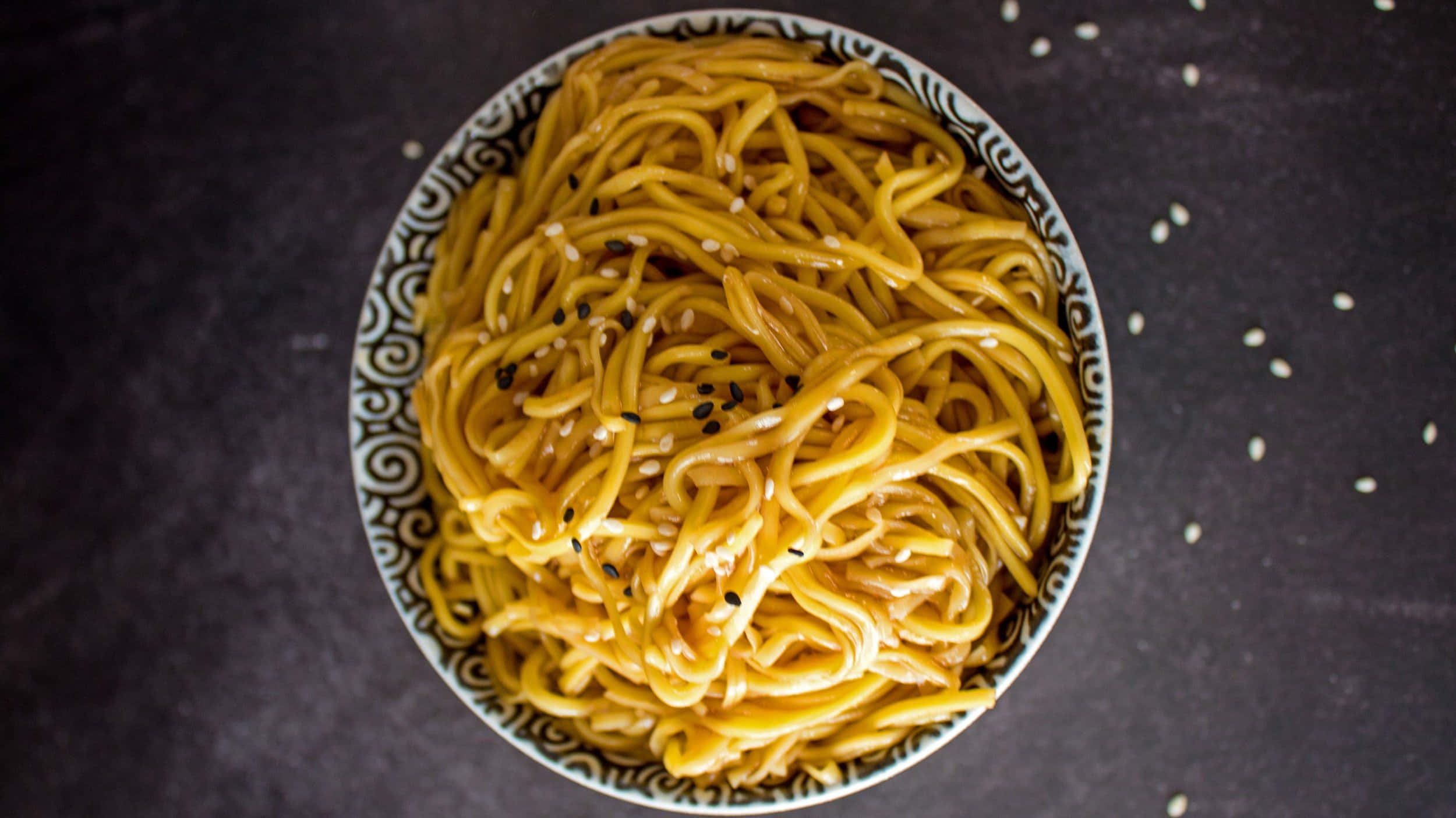 Food Photography 桌布 壁紙 — 金色麵條配上黑白芝麻，放在有圖案的碗中，置於深色表面上。