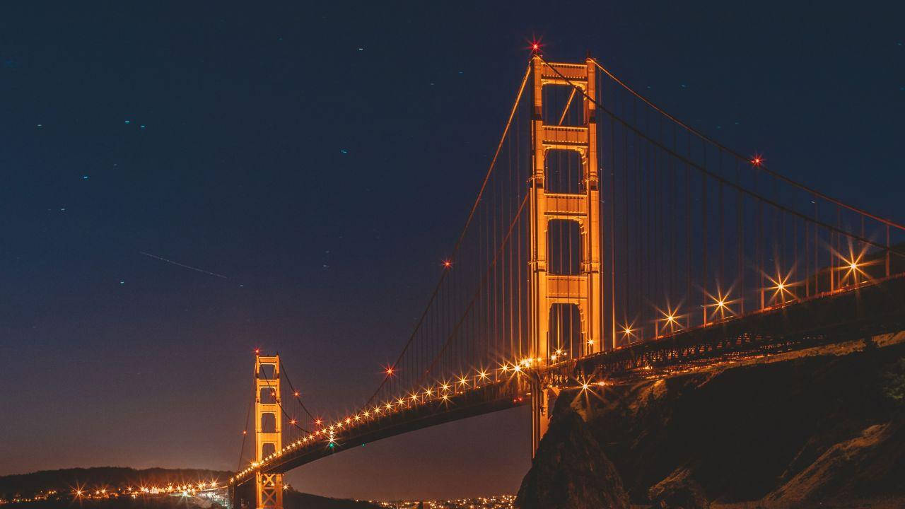 夜空 桌布 壁紙 — 金門大橋在夜晚被照亮，背景是星空，橋樑上閃爍著燈光。