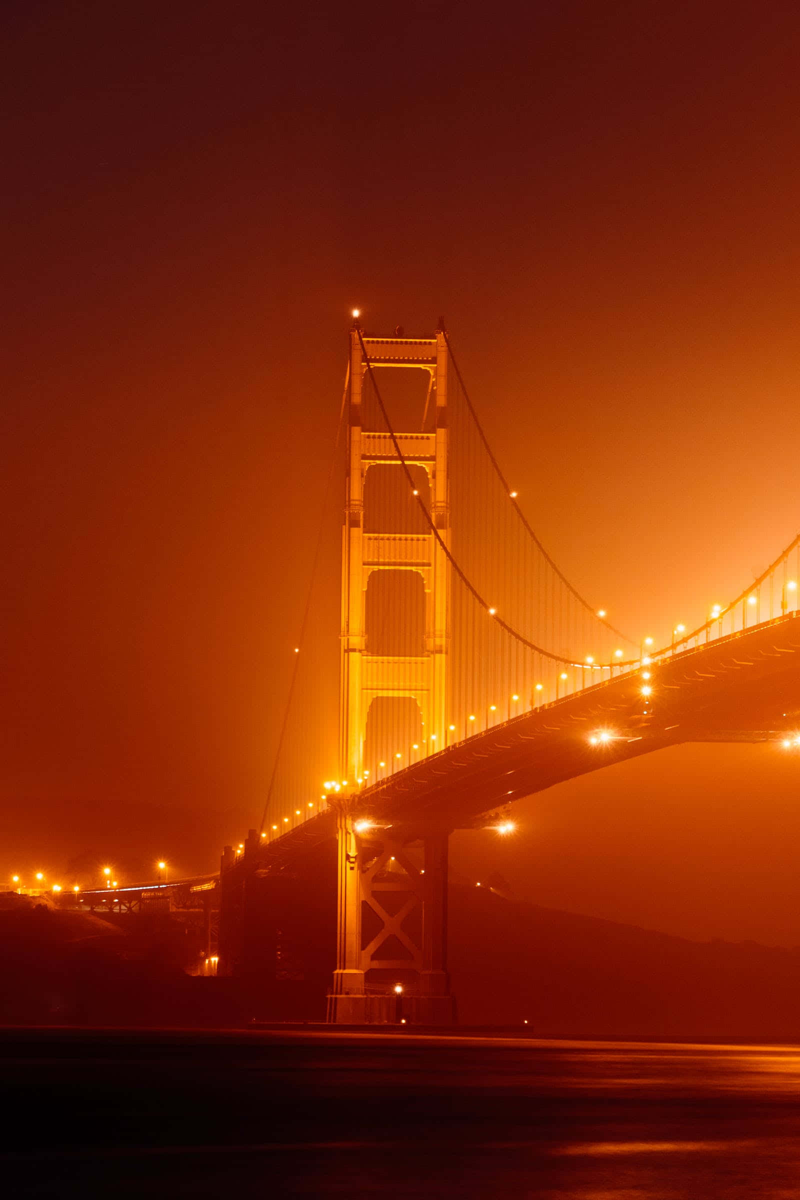 San Francisco Fog 桌布 壁紙 — 金門大橋在夜間濃霧中溫暖地發光，橙色燈光映照其結構，襯托著朦朧的天空。